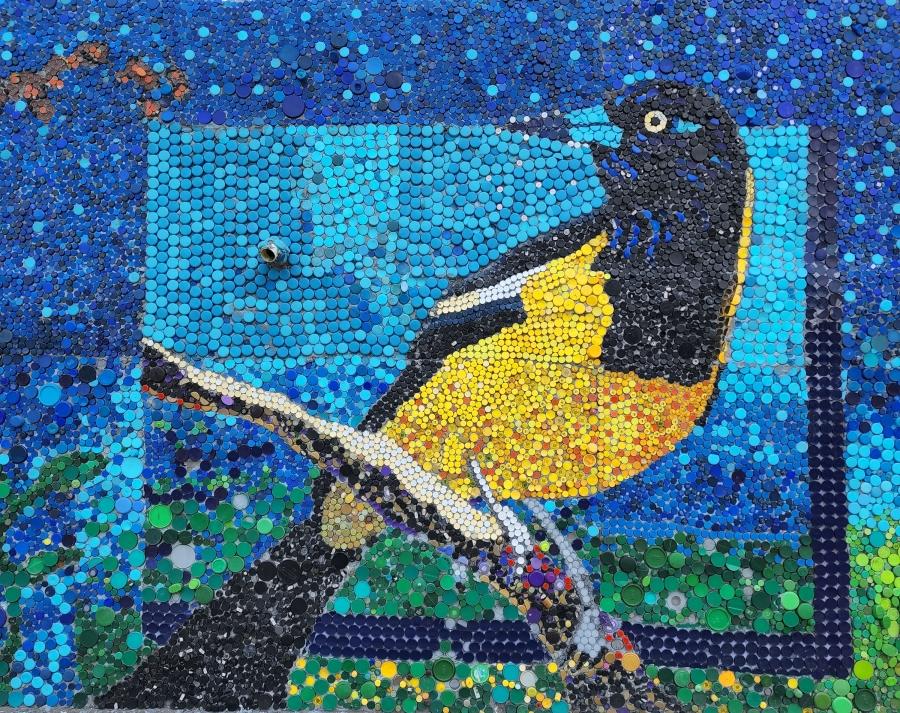 black and yellow bird standing on a branch with a blue background; this picture is made out of bottle caps