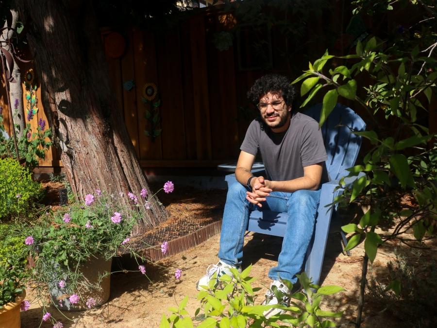 portrait of a man wearing a gray shirt and light jeans sitting in a garden