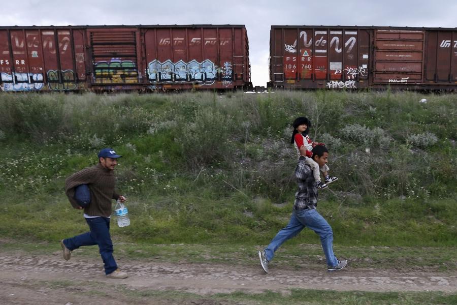 A Salvadoran father carries his son while running next to another immigrant as they try to board a train heading to the Mexican-U.S. border, in Huehuetoca, near of Mexico City, June 1, 2015.