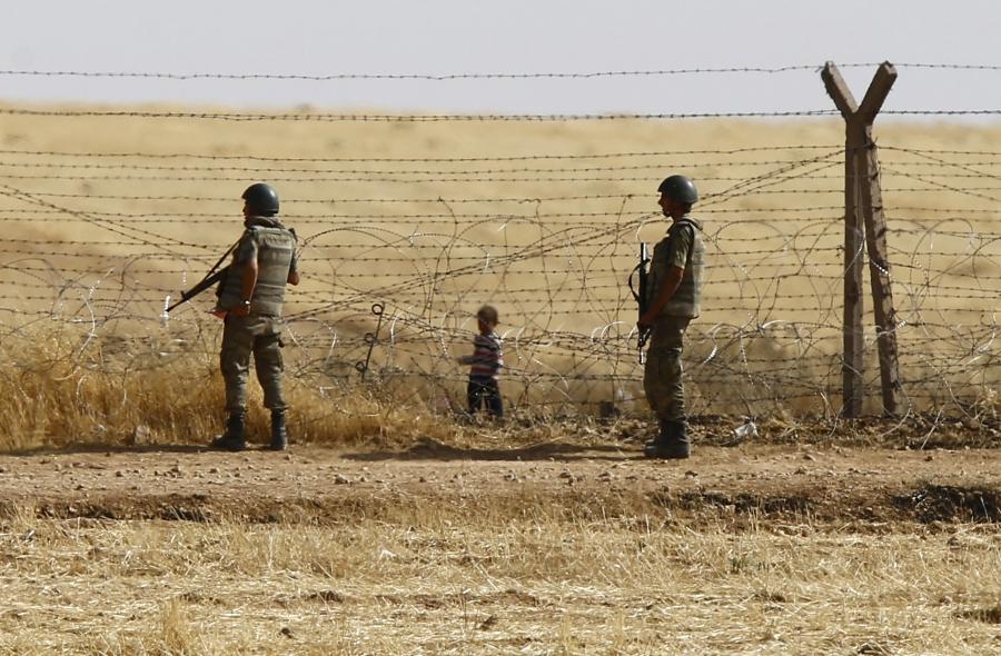 Turkish soldiers stand guard as a Syrian refugee boy waits behind the border fences to cross into Turkey on the Turkish-Syrian border, near the southeastern town of Akcakale in Sanliurfa province, Turkey, June 5, 2015.
