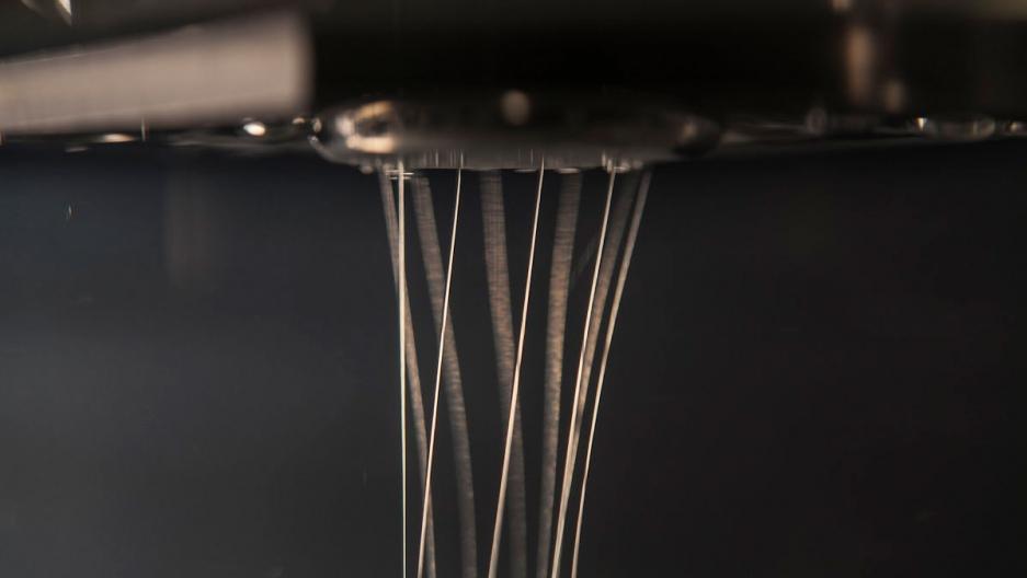 Very thin fibers, almost like fishing line, dangle from the top of a machine in this close-up image of the spider silk technology.