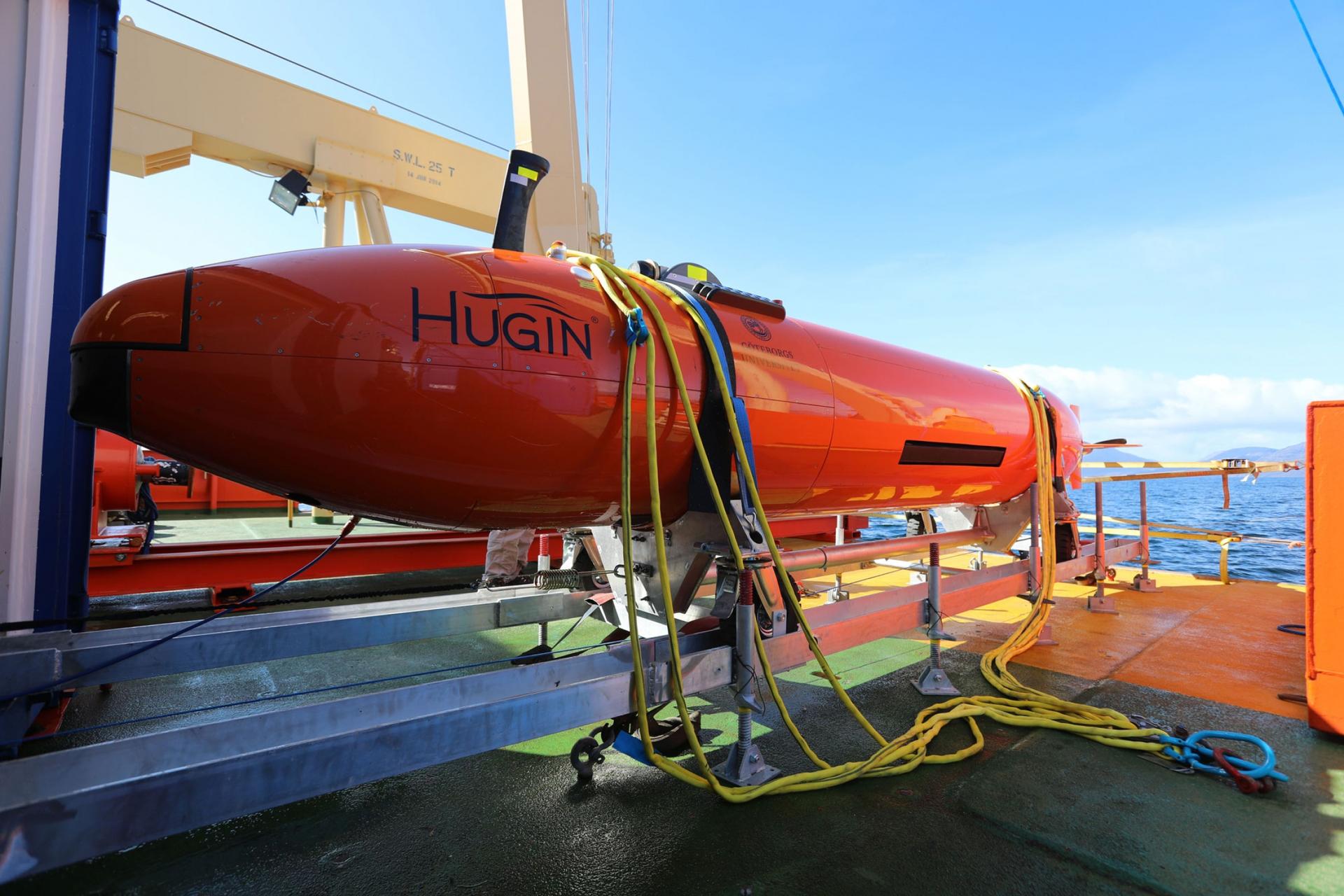 The Hugin, a long orange metal submarine is shown on the deck of the ship.