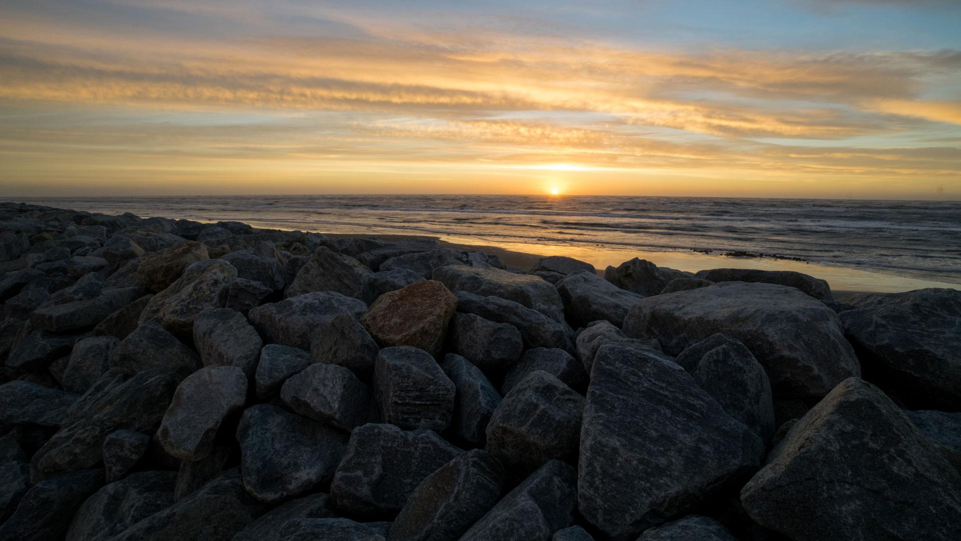 The sun sets into the ocean along a rocky seawall