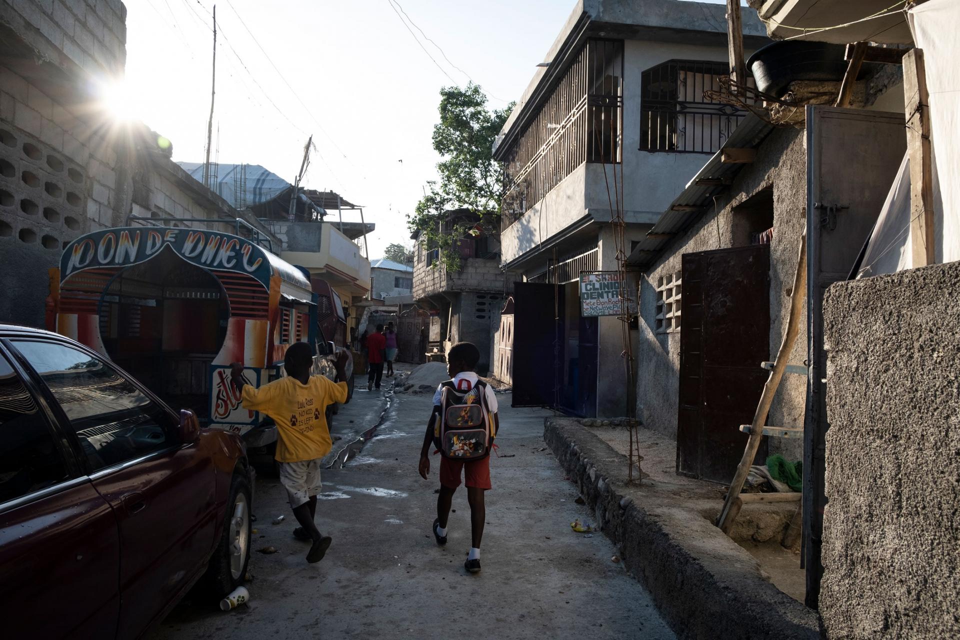 Two children, one with a backpack, are shown walking through a neighborhood in Laboule, outside of Port-au-Prince, Haiti.