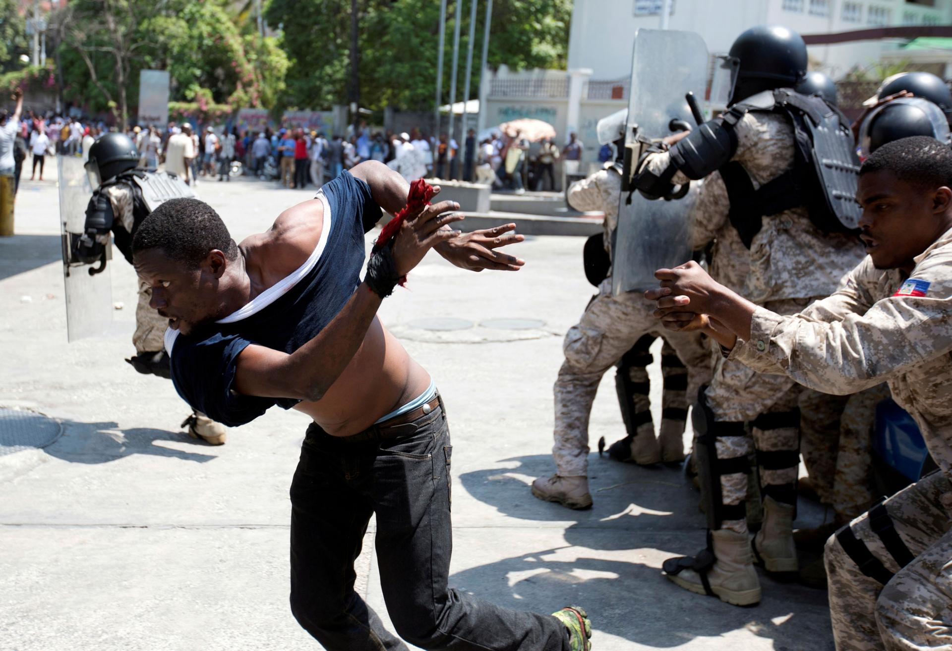 A demonstrator is shown running from Haitian security authorities with his blue shirt almost torn off.