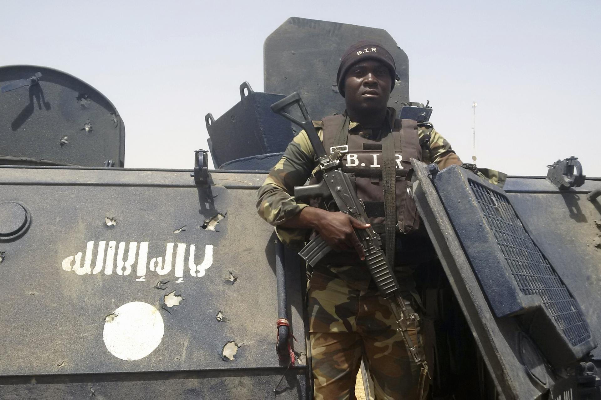 Cameroonian soldier stands near tank with Boko Haram logo on it. 