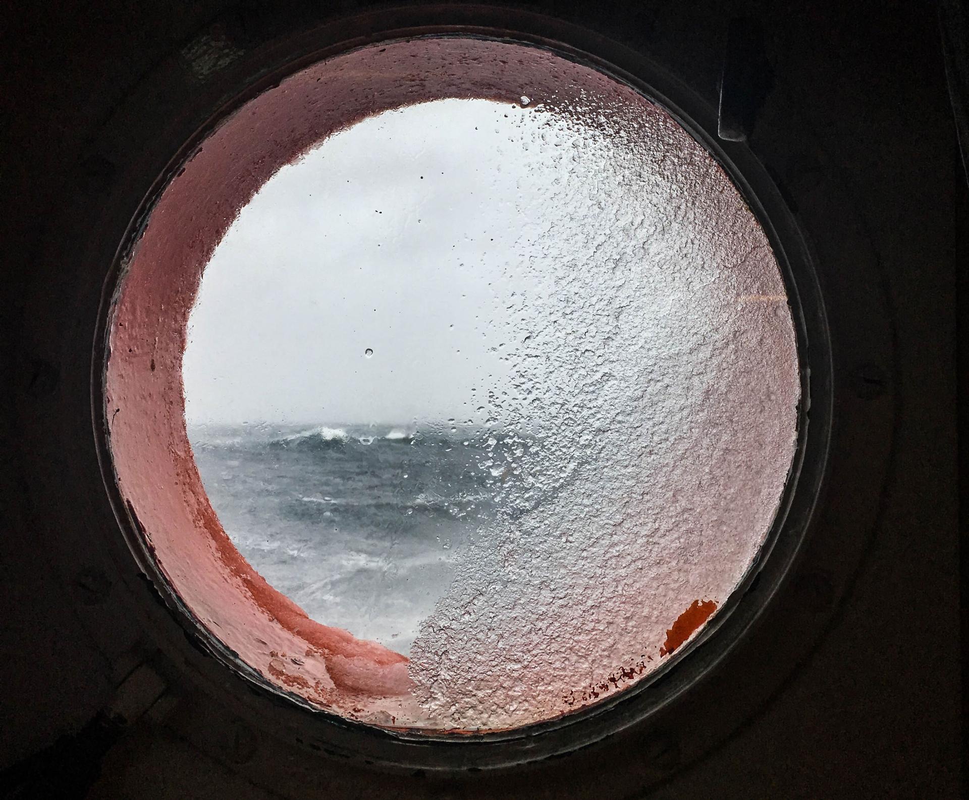 A round window is shown with very choppy waves off in the distance.