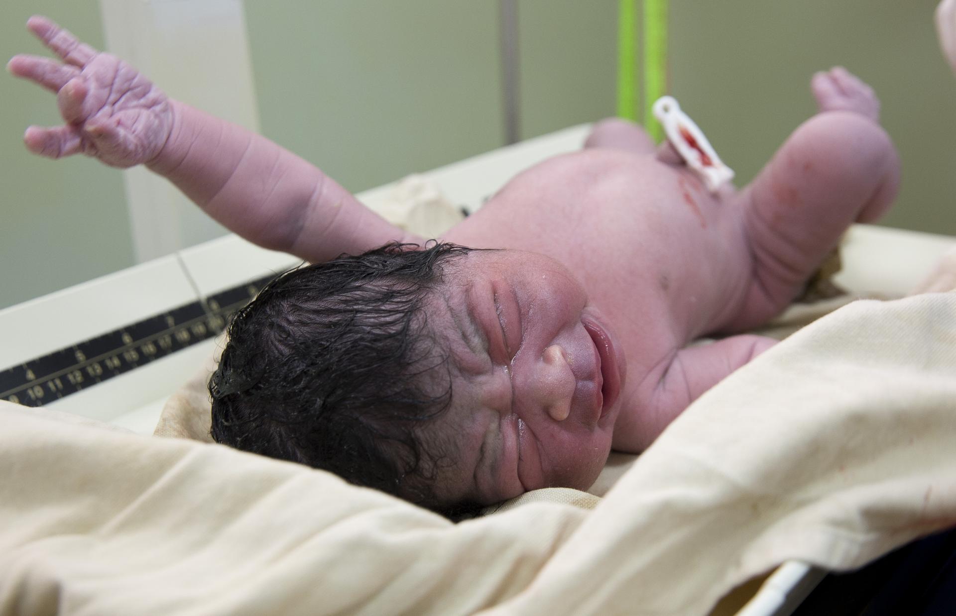 newborn baby with black wet hair and fist raised and clipped belly button