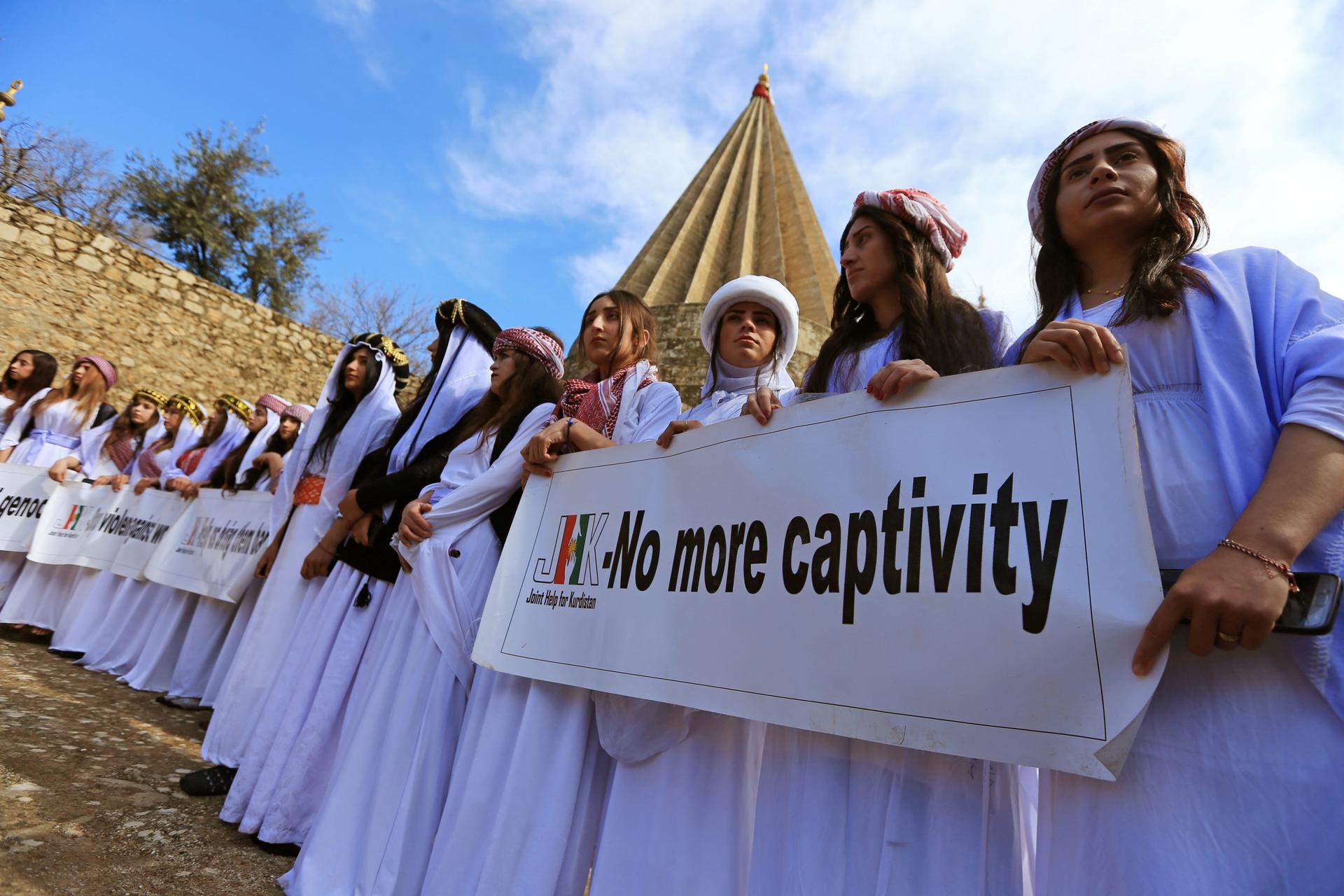Women in white robes and turbans carry sign that says "no more captivity." 