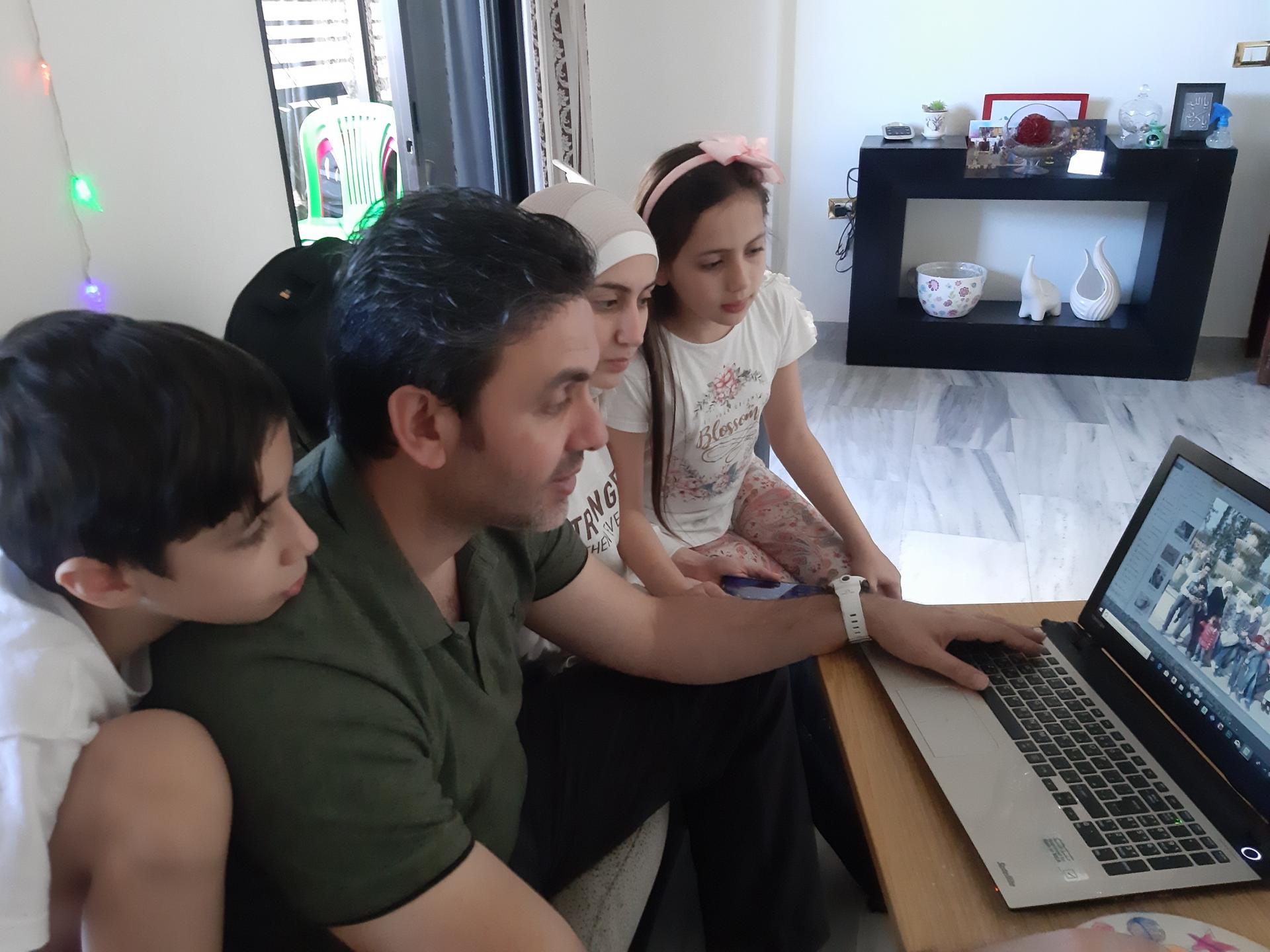 A man looks at photos on a laptop screen with his children