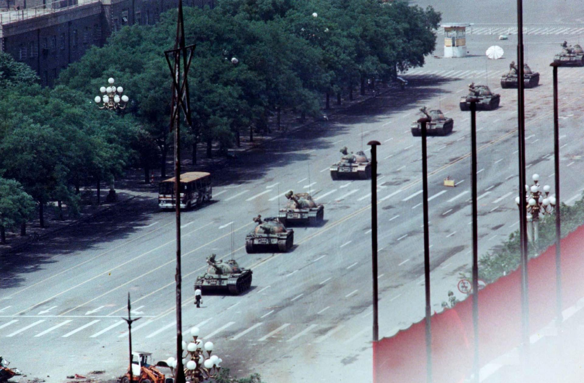 A man defiantly stands in front of a line line of tanks. 