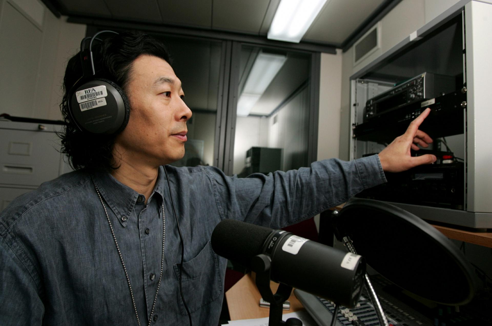 A man with headphones on speaks into a microphone in a studio. 