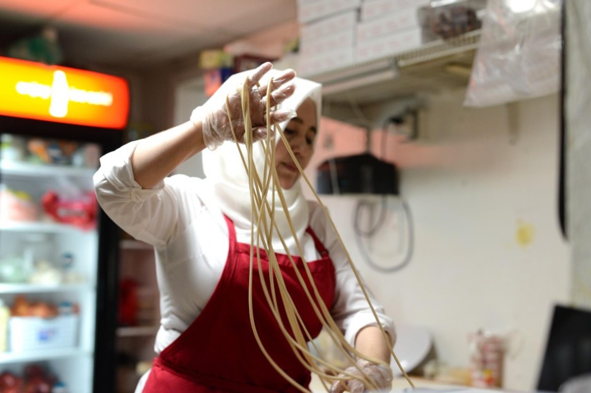 A woman in a kitchen makes noodles. 