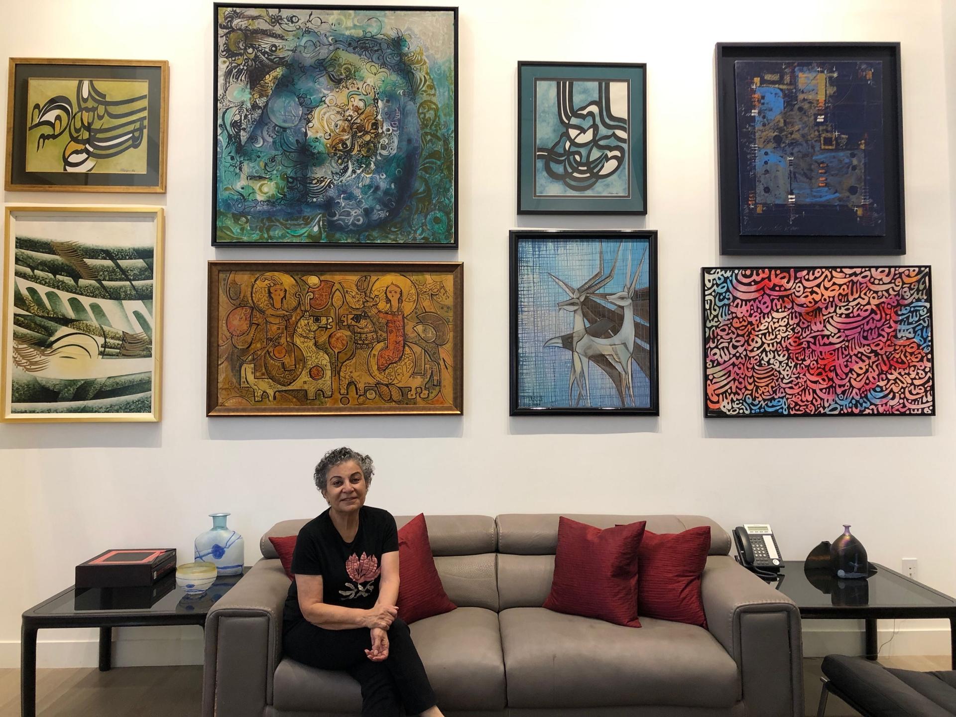 A woman sits on a couch with several works of art behind her.