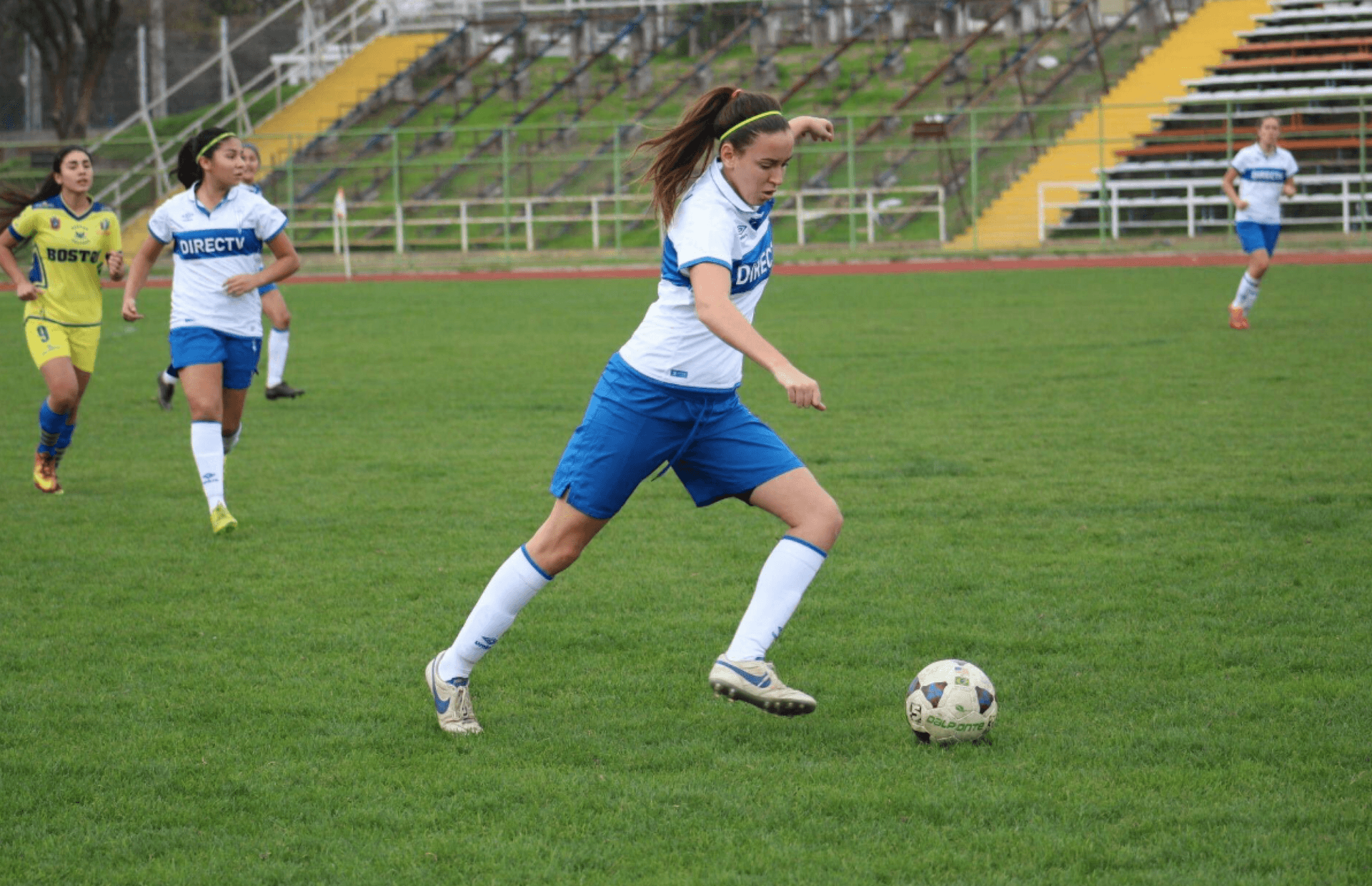 A woman wears a blue and white uniform and kicks a soccer ball.