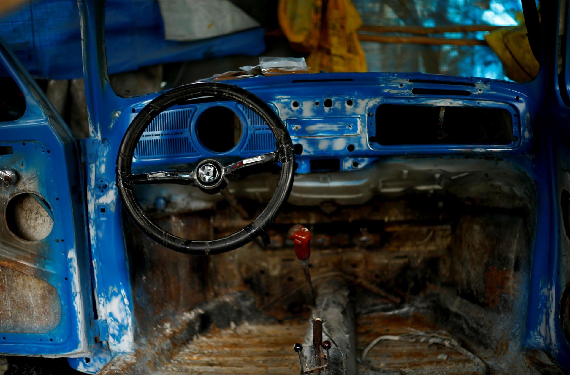 The blue, stripped down interior of a Volkswagen Beetle car is shown along with a black steering wheel.