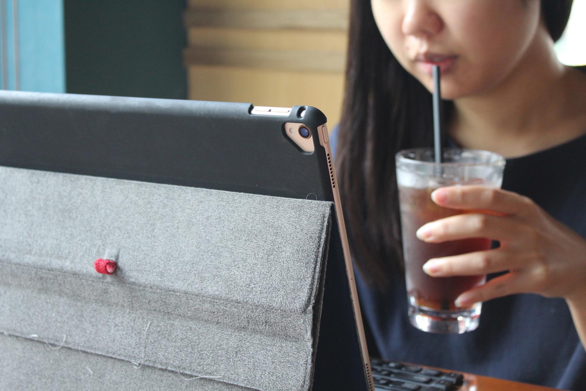 A woman sips a cold drink while looking at her laptop screen