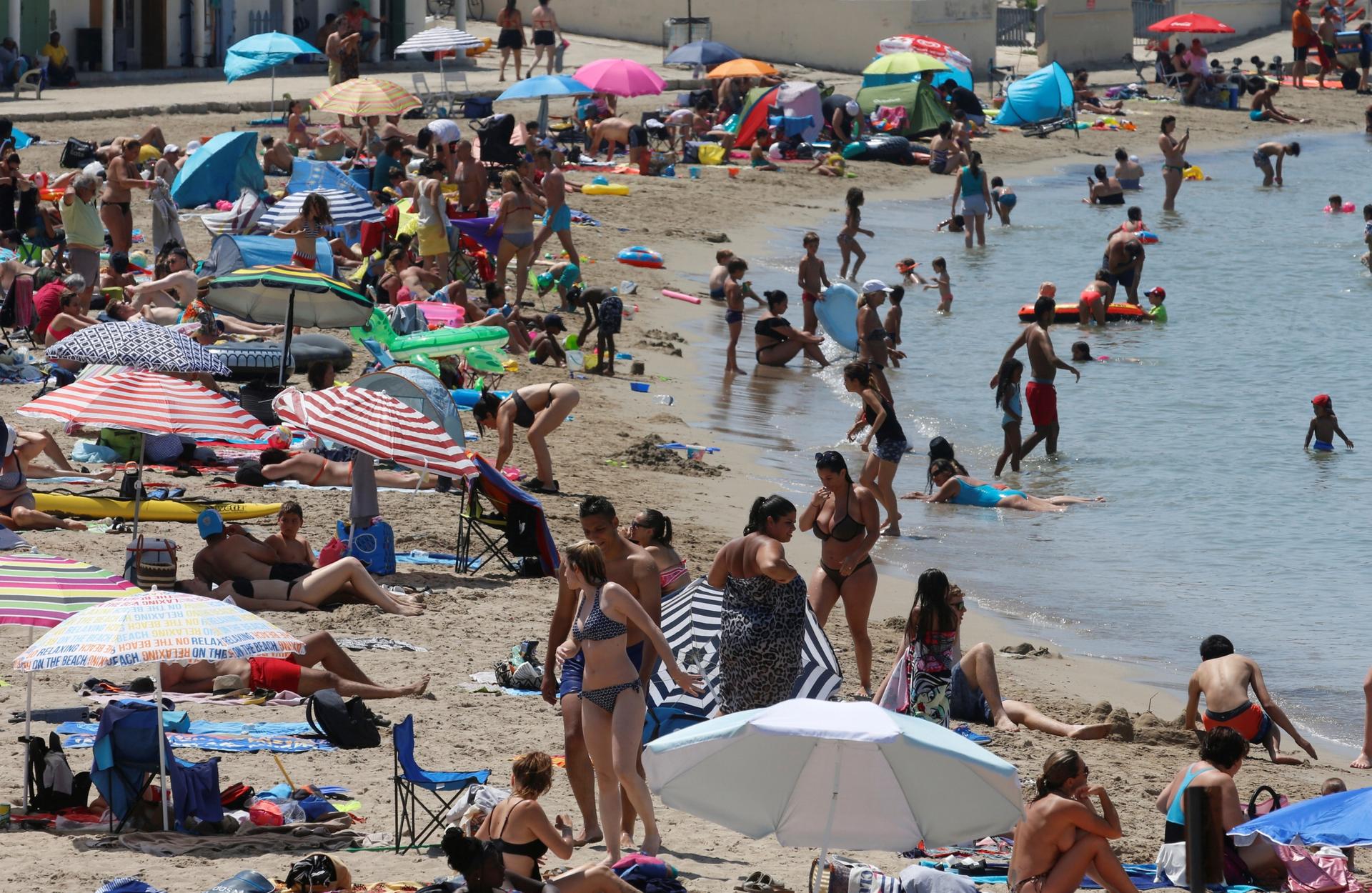 A stretch of crowded beach with lots of colorful umbrellas and people in bikinis
