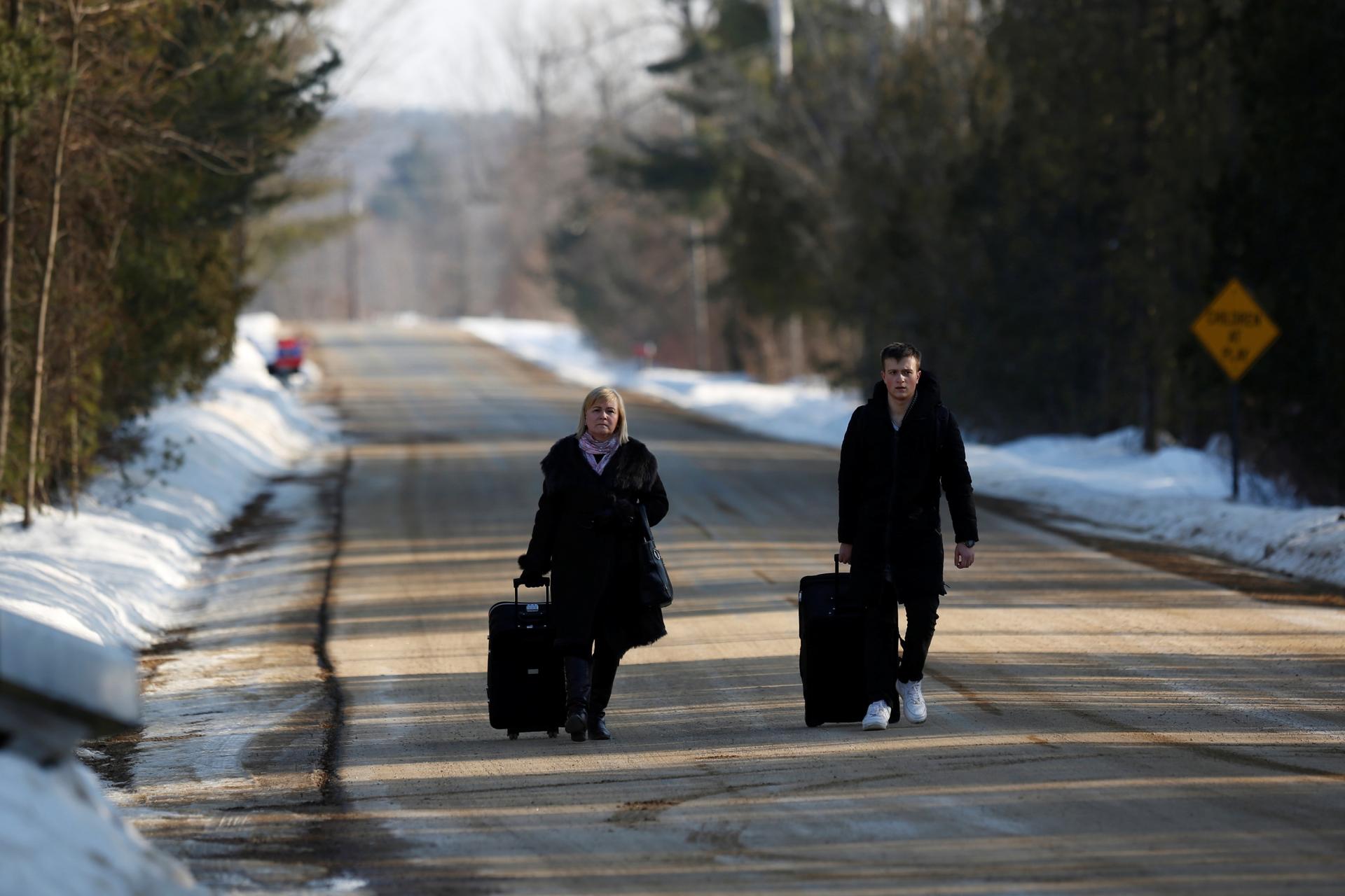 Two people walk with luggage along an empty road