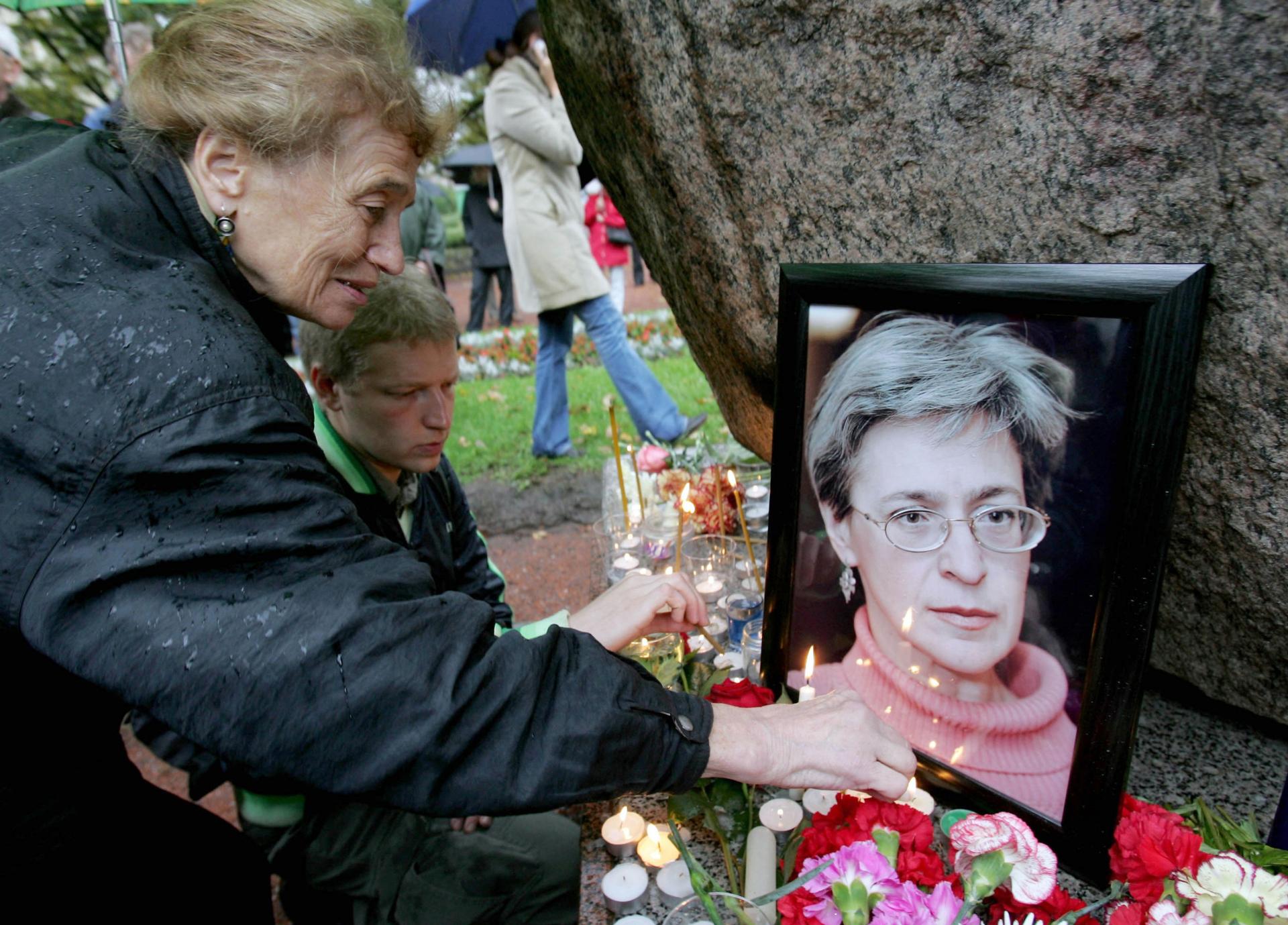 A woman lights a candle next to a framed image of Russian journalist Anna Politkovsaya