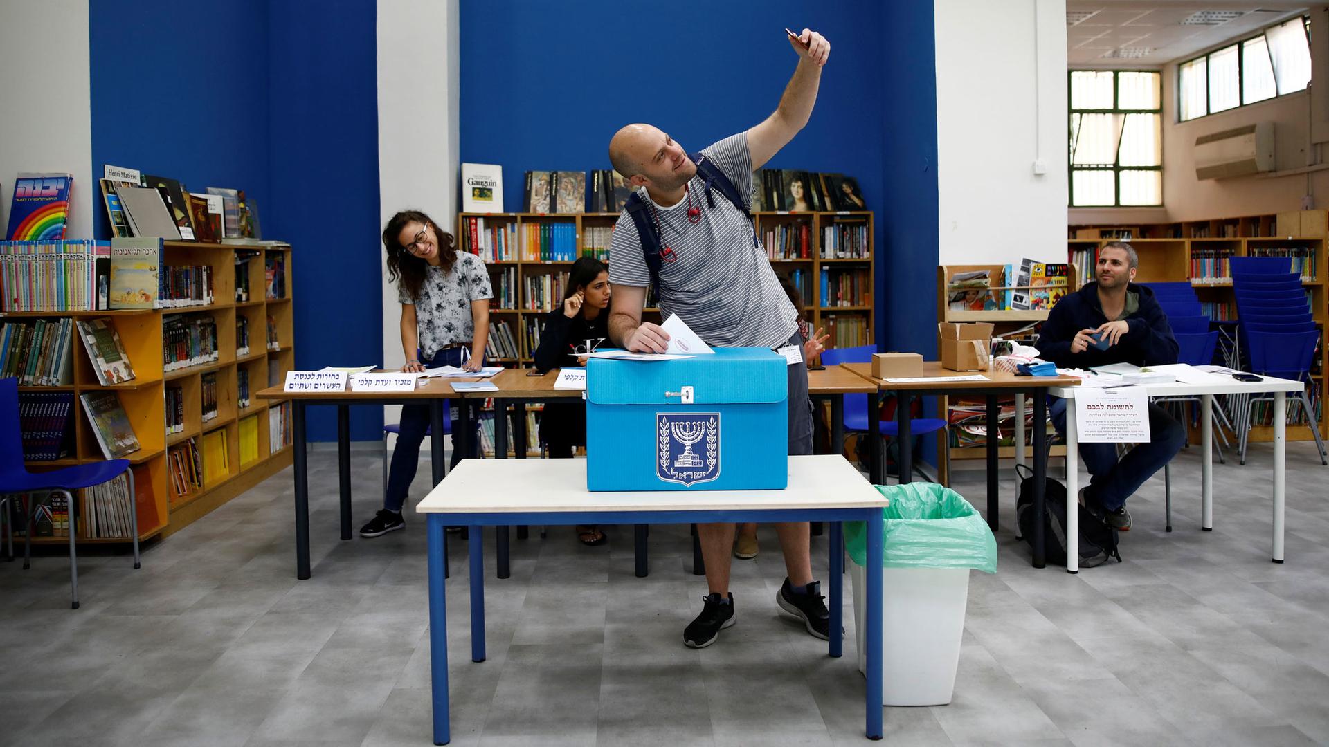 A man holds his cell phone above his head for a selfie with the ballot box 