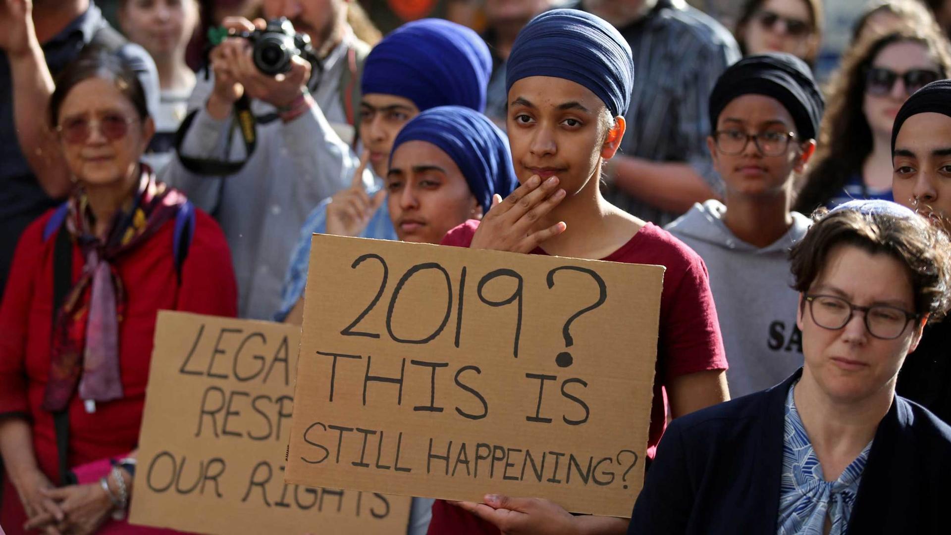 Protesters hold signs that 2019? This is still happening? 