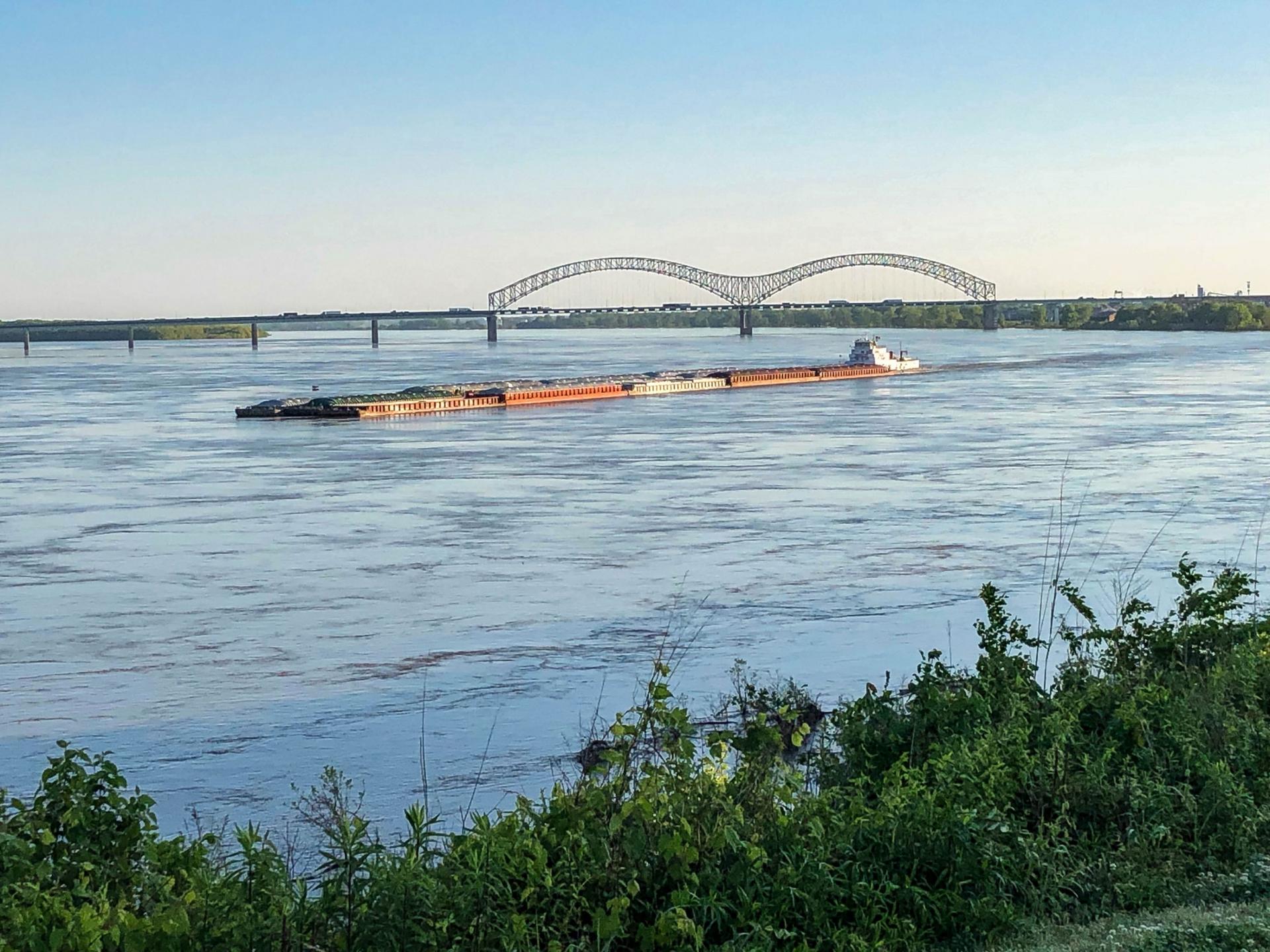 A barge is shown in the distance traveling on a blue river.