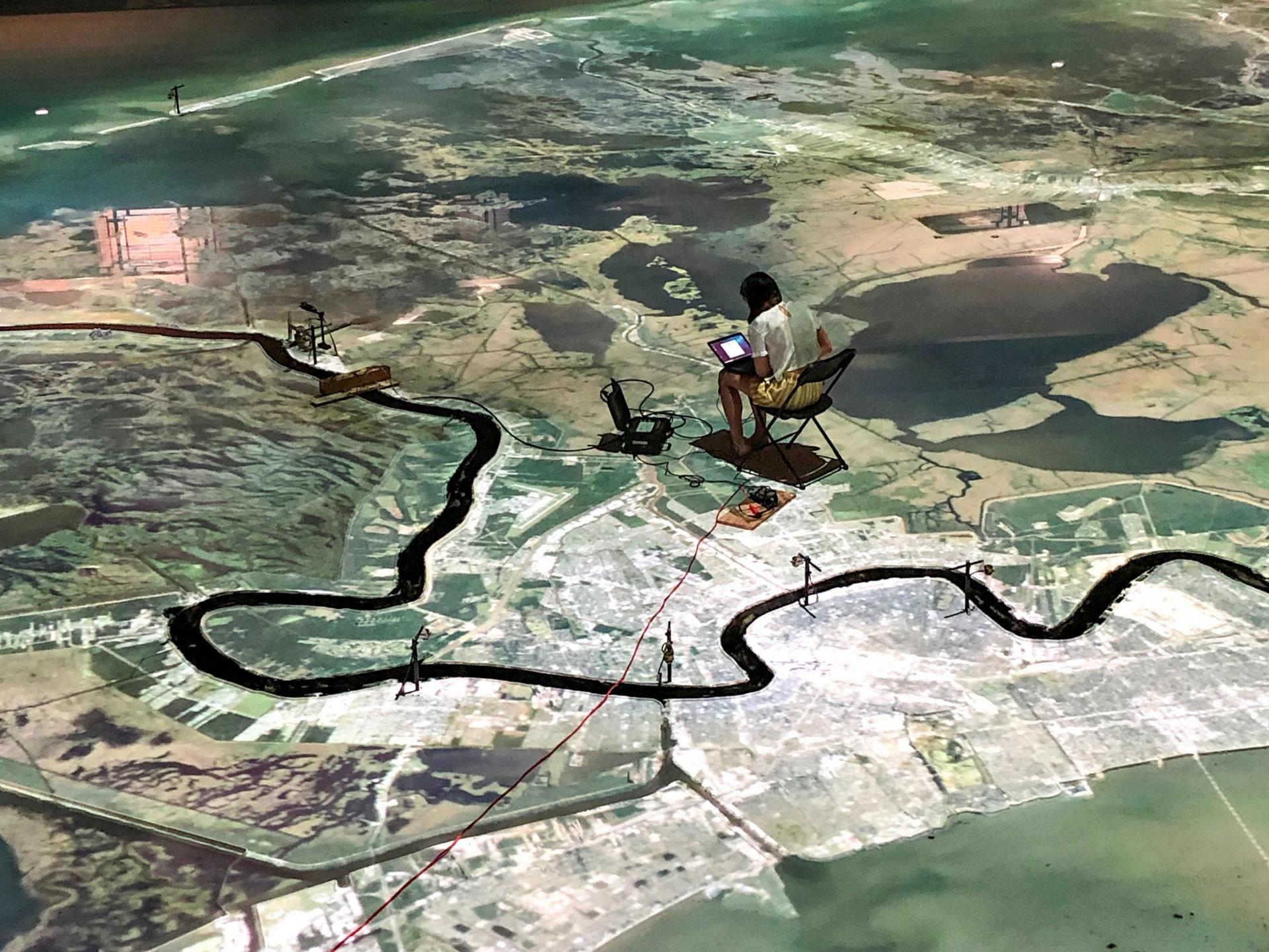 A large scale map of the Mississippi River is shown from above with a person sitting in a chair on the map.