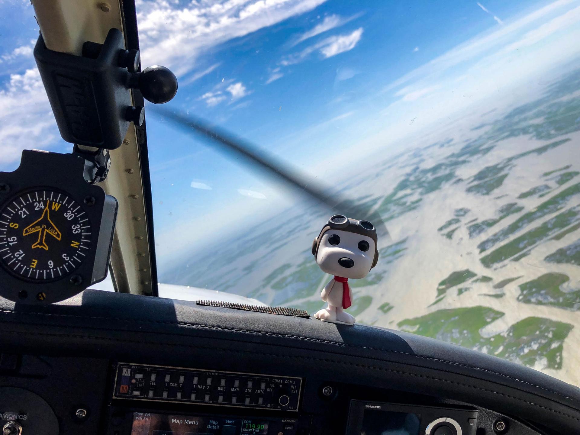 A figurine of Snoopy is shown on the dashboard of four-seat plane with aviator attire.