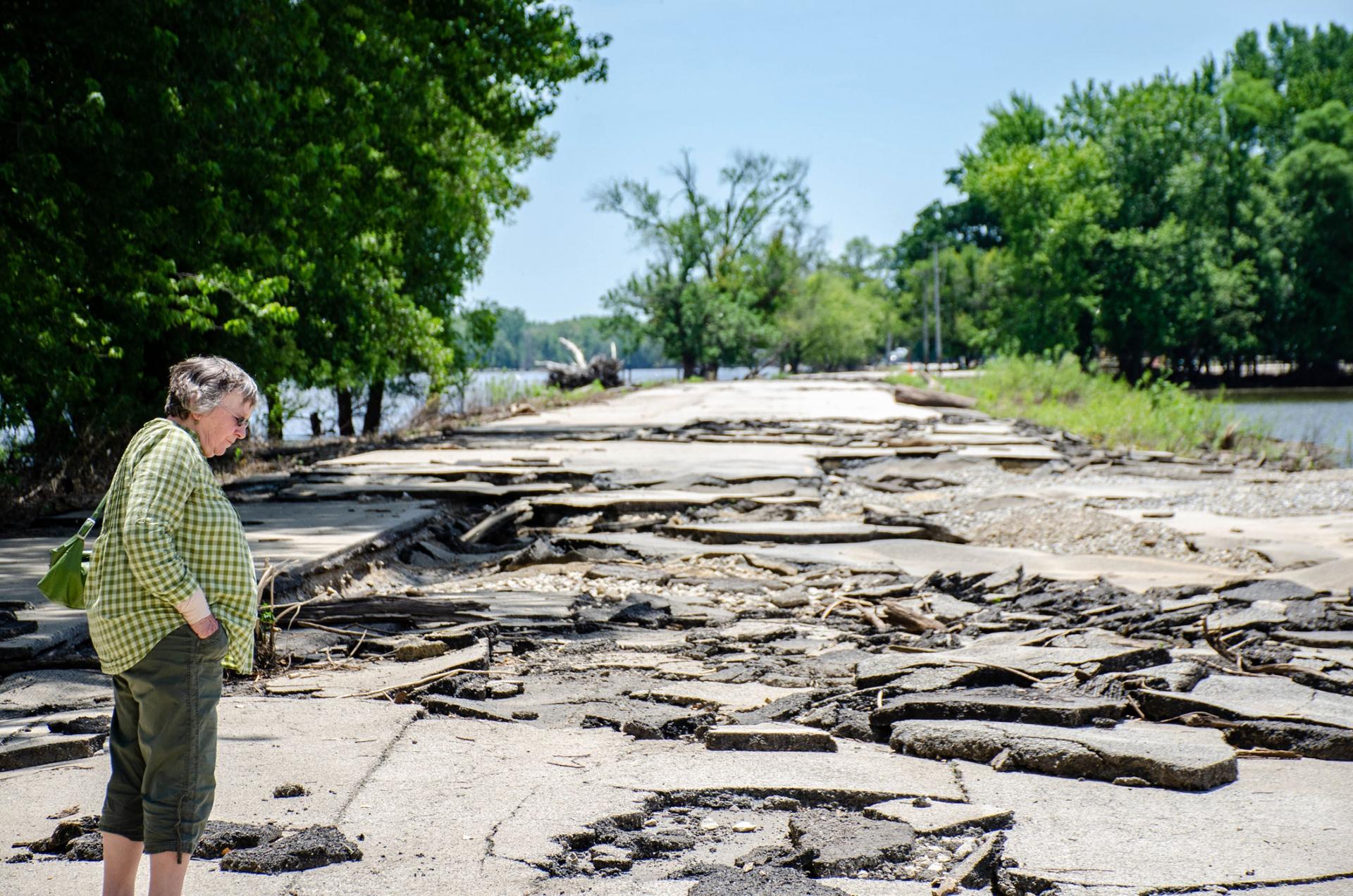 A woman is shown standing on a road that is broken up in many pieces.
