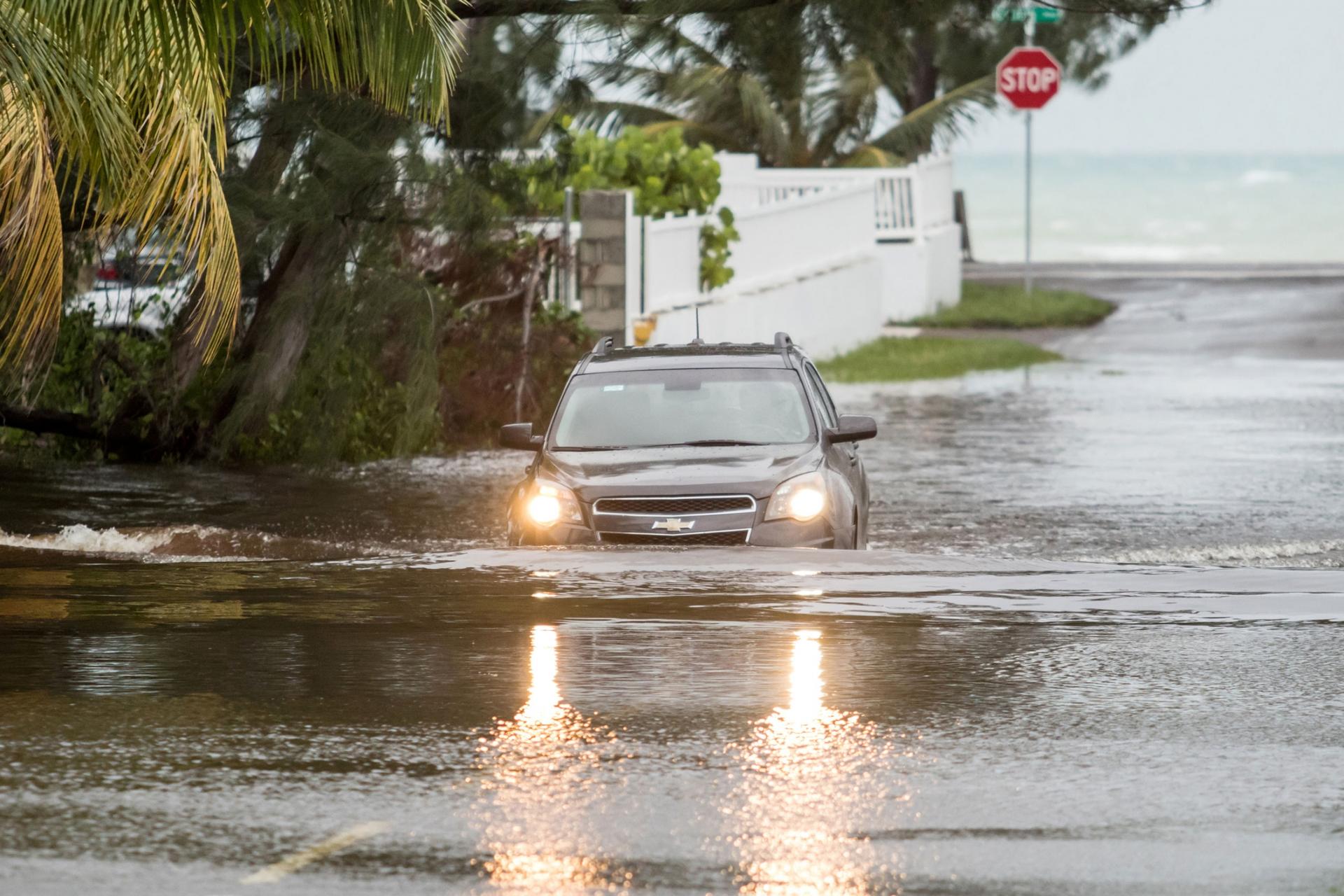 A Chevy SUV is shown driving with its lights on in a flooded street with water halfway up the tires.