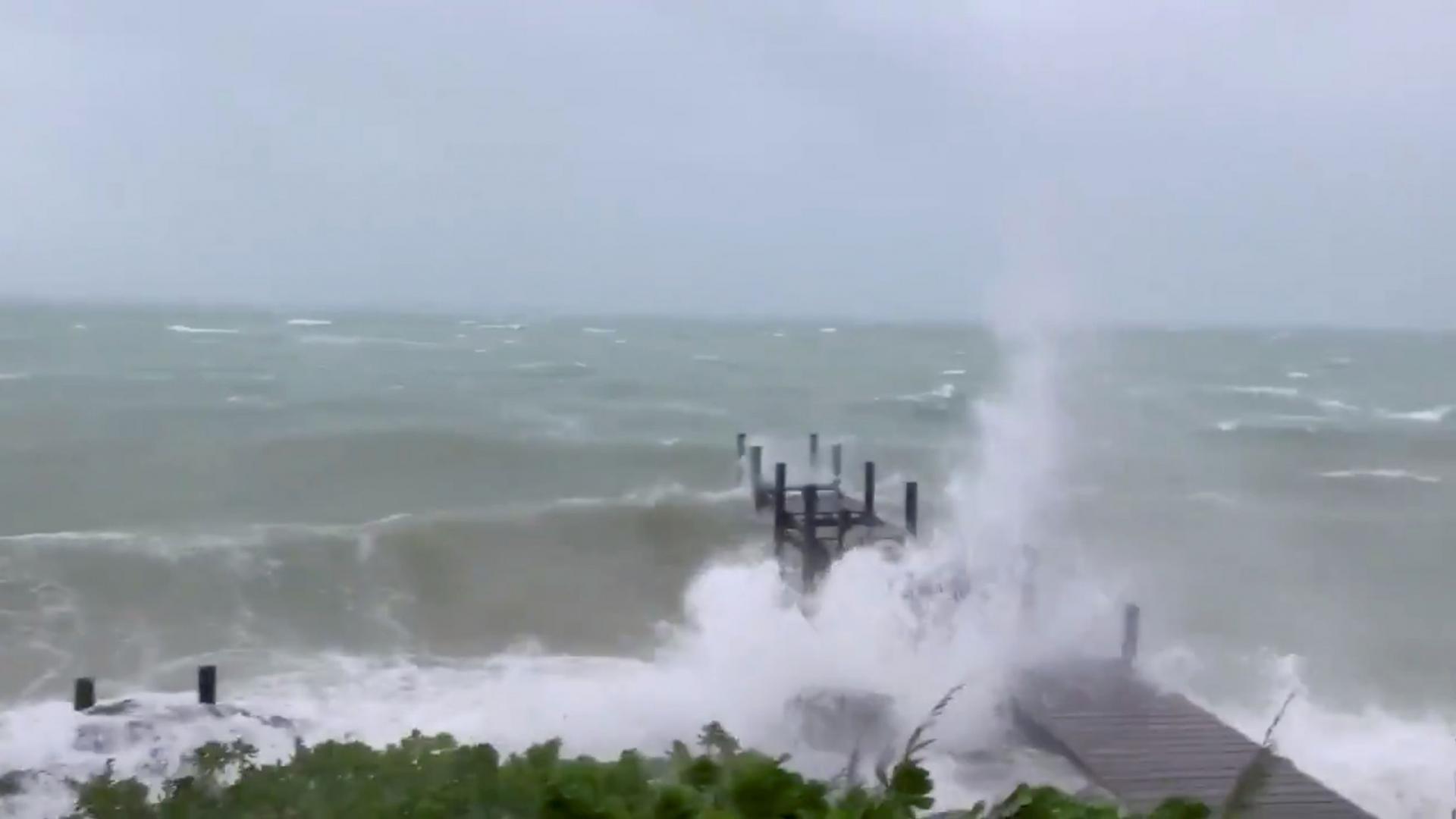 Waves are shown crashing into a dock jutting out into the ocean.
