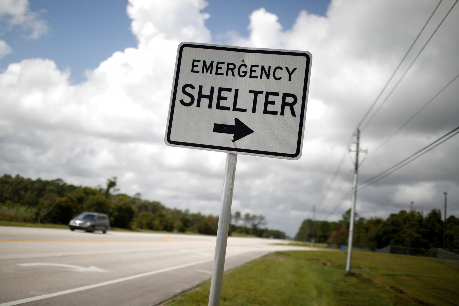 A street sign is shown next to a road with "Emergency Shelter" and an arrow pointed to the right printed on it.