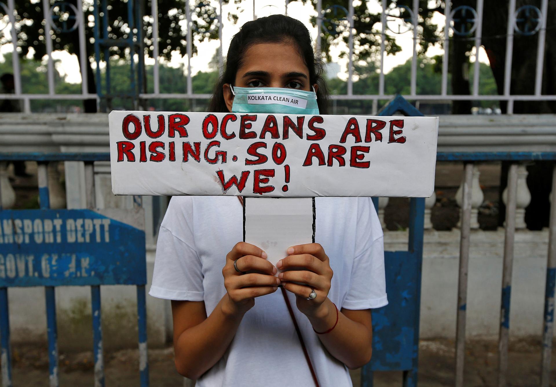 A woman is shown standing and holding a sign that reads, "Our oceans are rising. So are we!"