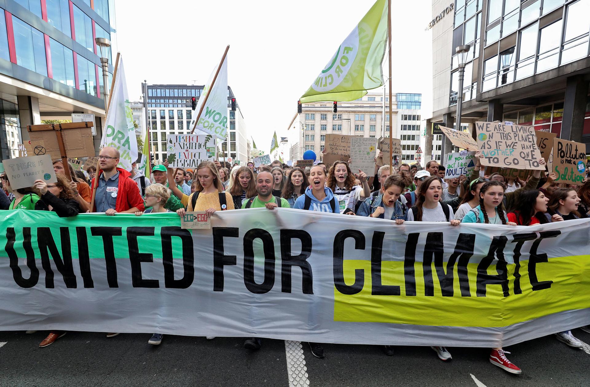 A large group of people are shown in the street with a long banner that reads, "United for Climate."