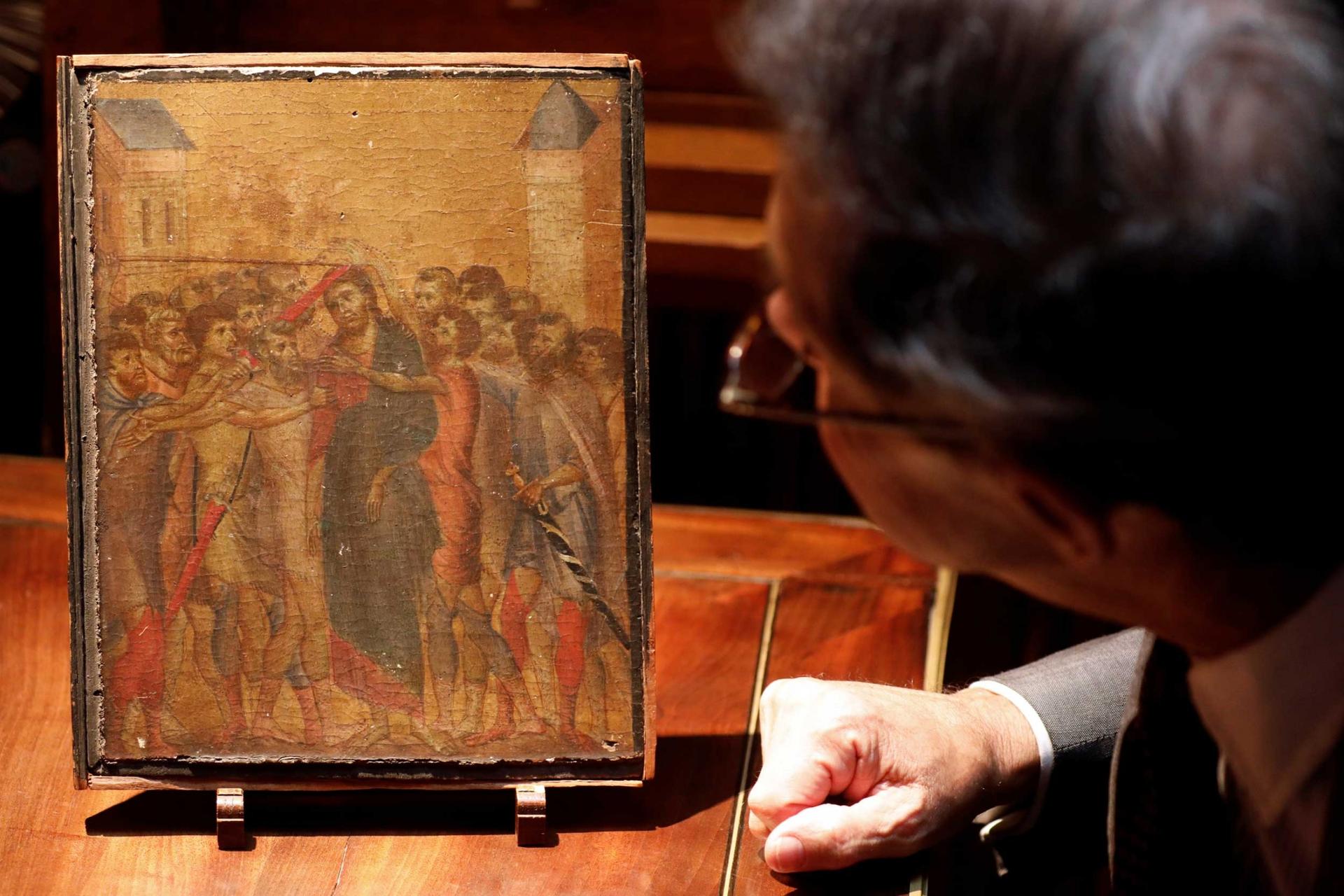 A man looks closely at a small religious image showing Christ surrounded by other men