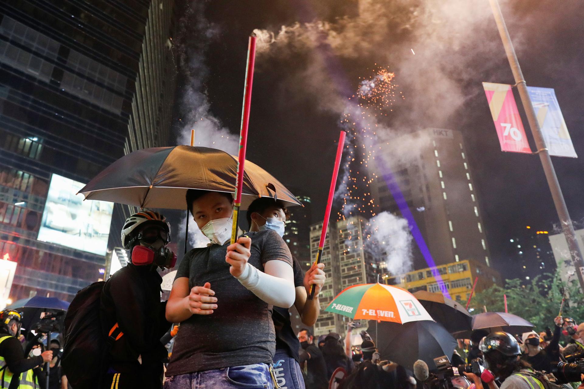 A group of protesters are shown with umbrellas and holding fireworks.