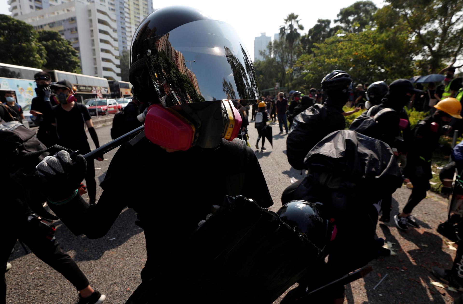 A protester is shown wearing a helmet with a reflective face shield and a pink gas mask.