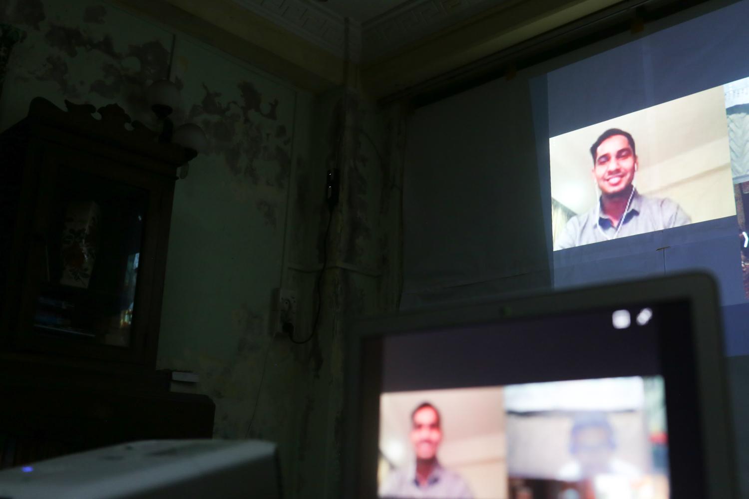 A man appears on a large screen wearing headphones in a video call