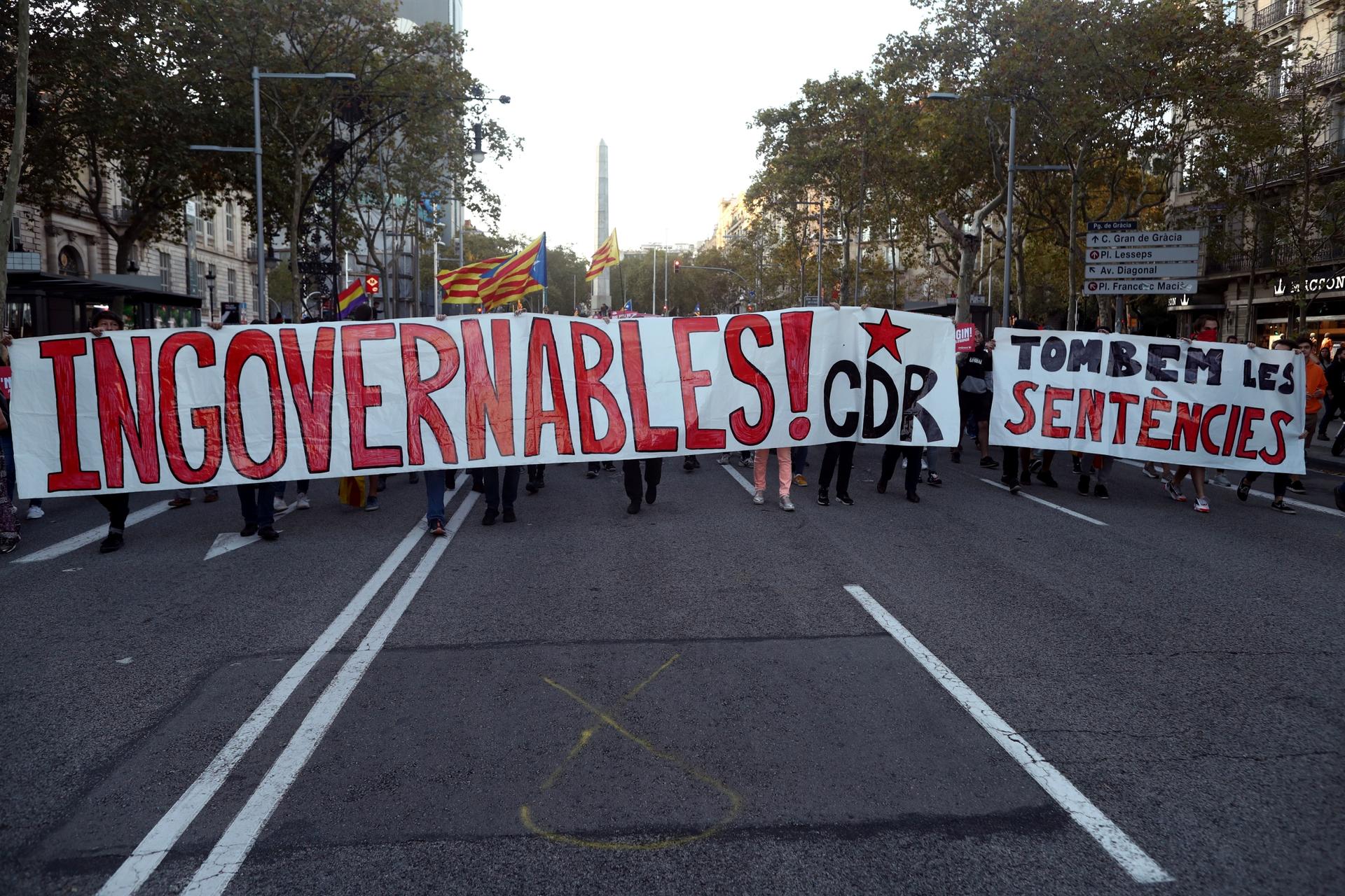 A group of protesters hold a large sign with red lettering on white cloth