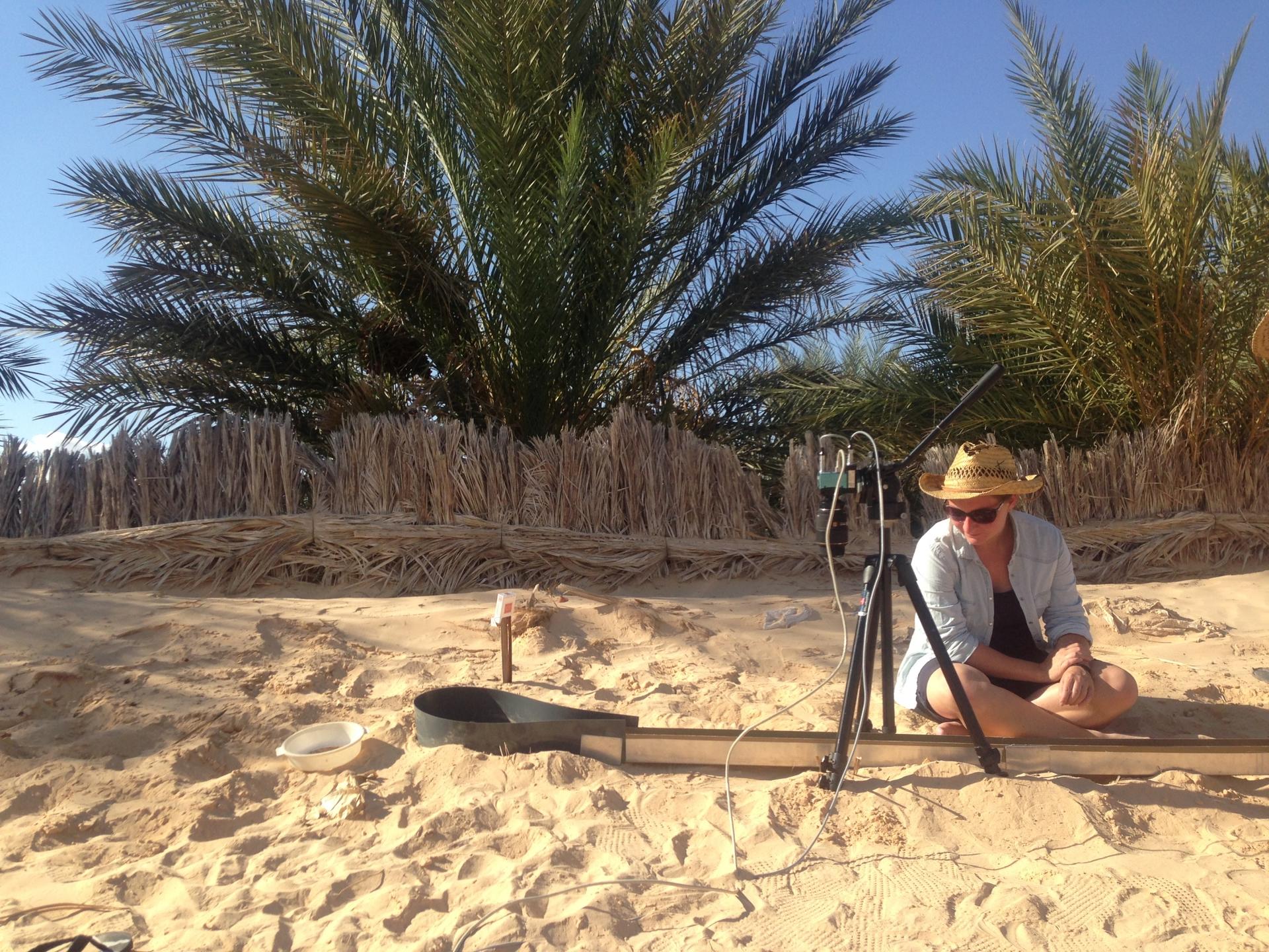 A person wearing a sun hat sets up a metal contraption in the sand. 