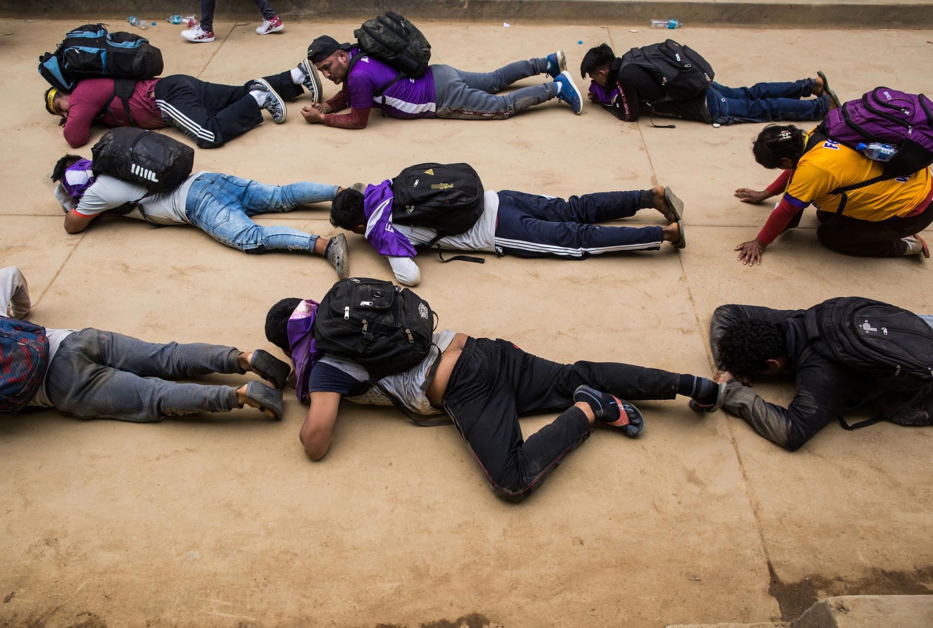 Several people are shown crawling on their stomachs on the ground and wearing backpacks.