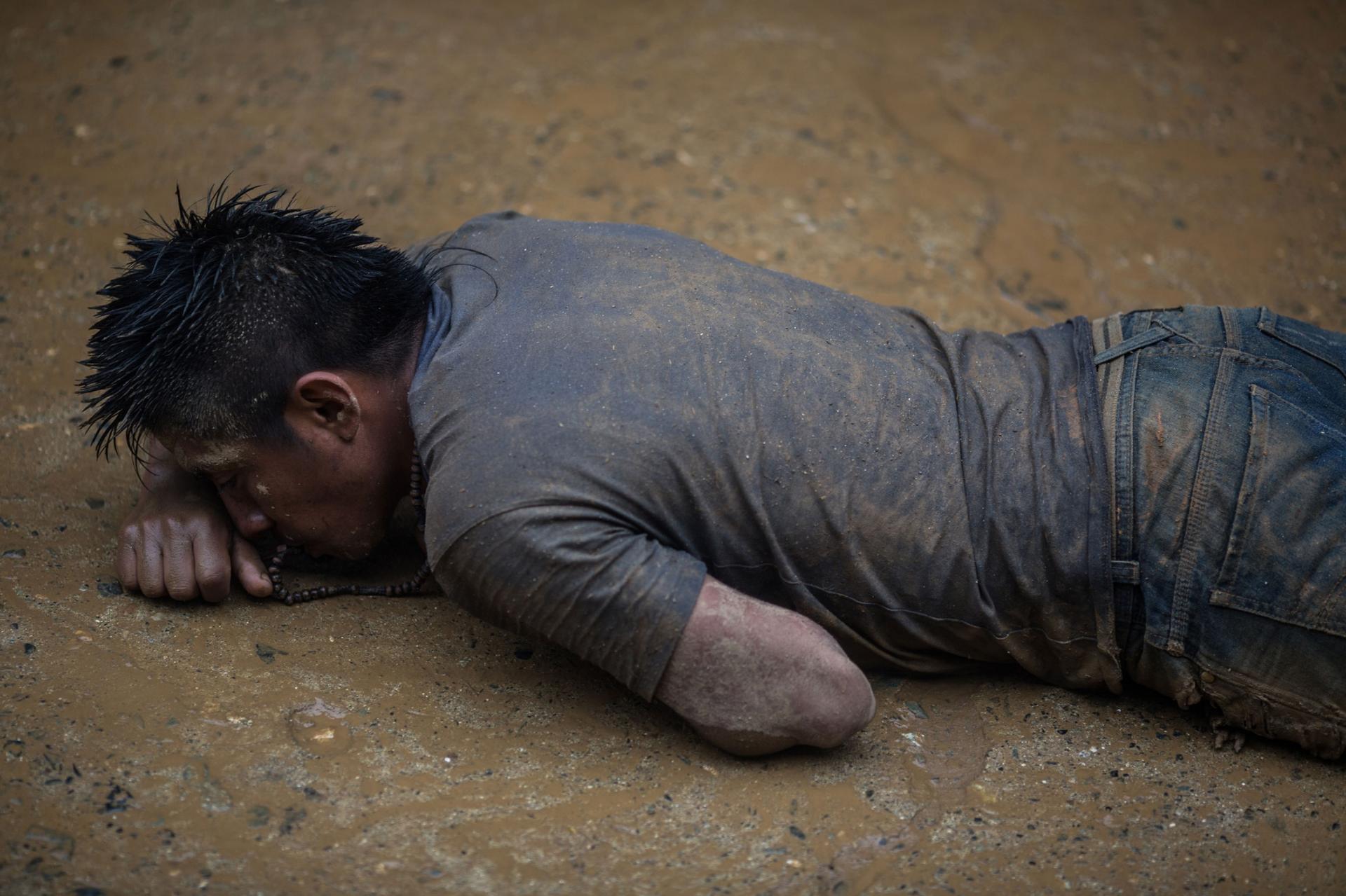 A man is shown crawling on his stomach in the mud and covered in dirt.