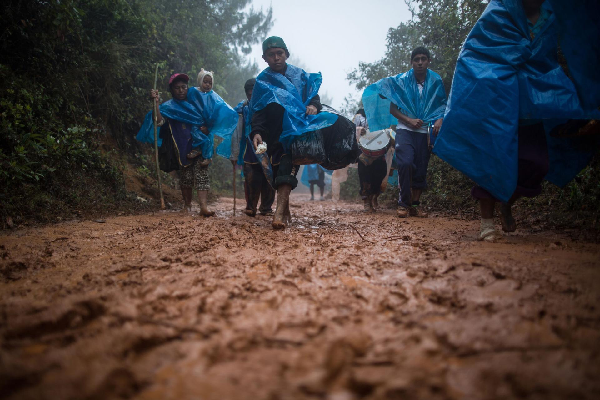 Several people are shown walking along a muddy path and wearing blue rain ponchos.