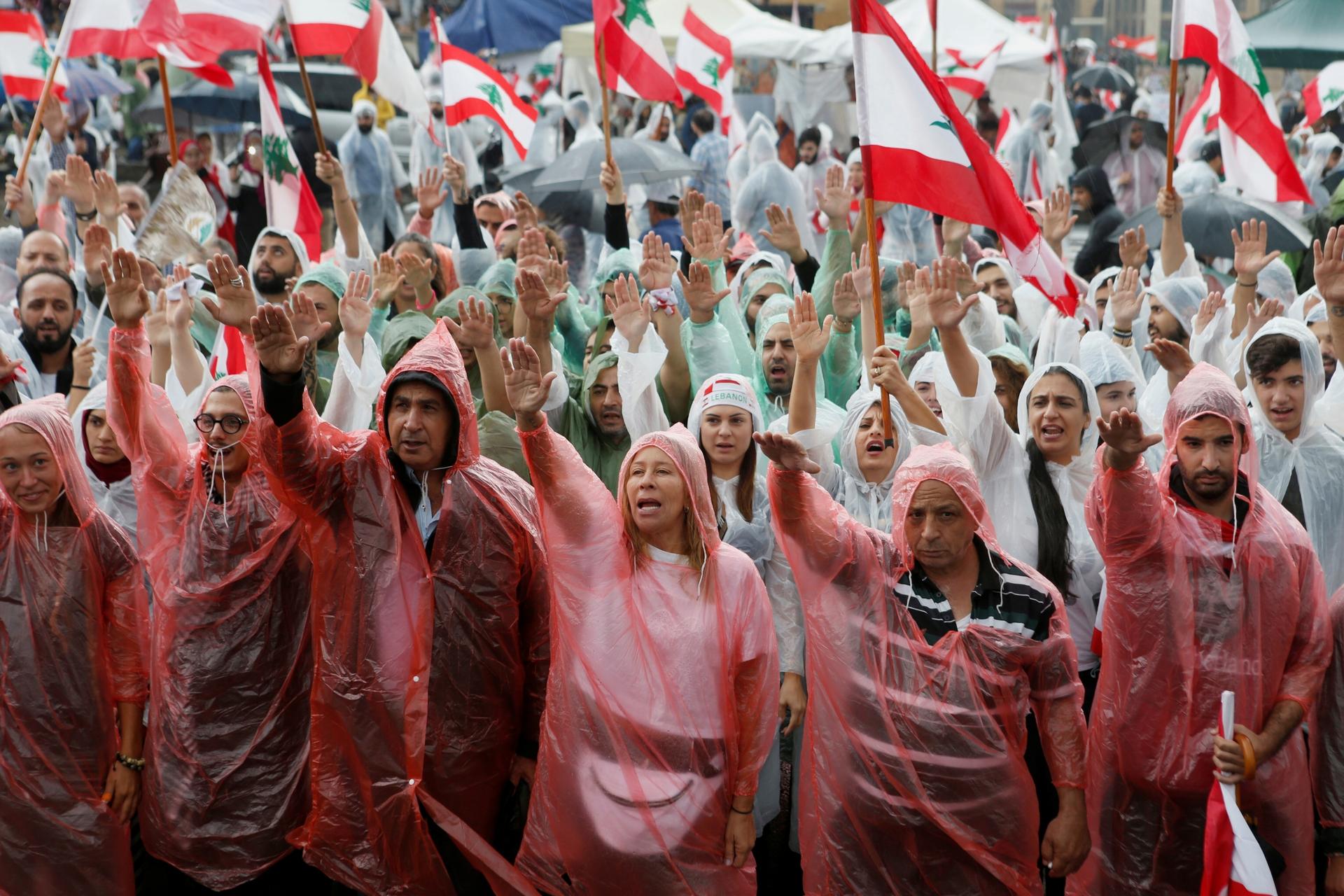 Demonstrators, covered in rain coats, gesture and carry flags during ongoing anti-government protests in downtown Beirut, Lebanon, Oct. 24, 2019. 