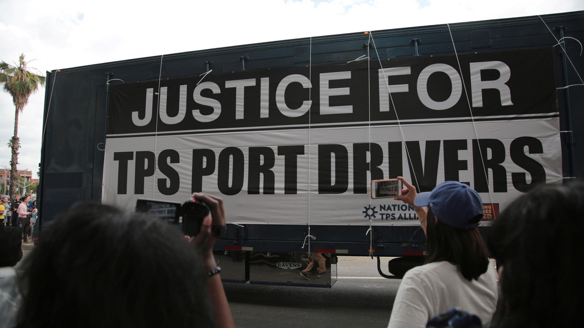 A large sign hanging off the side of a tractor reads "Justice for TPS Port Drivers" 