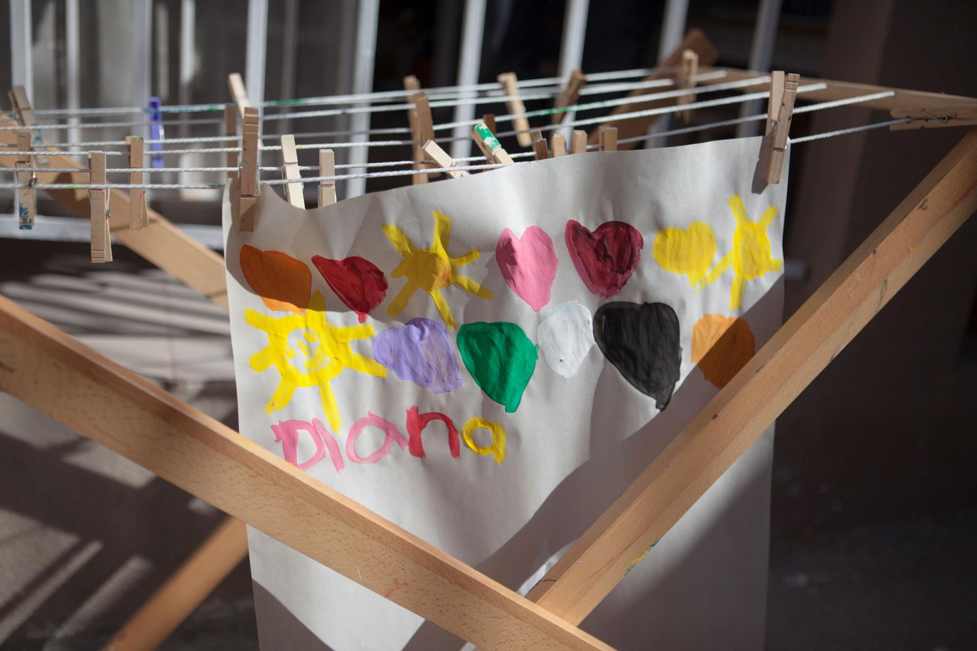 A white paper is shown with colorful hearts painted on it hanging from a wooden rack.