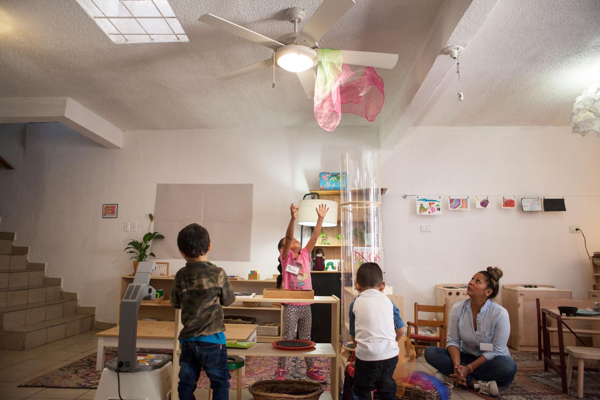 Several children are shown playing with a pink and white scarf shown caught attached to a ceiling fan.