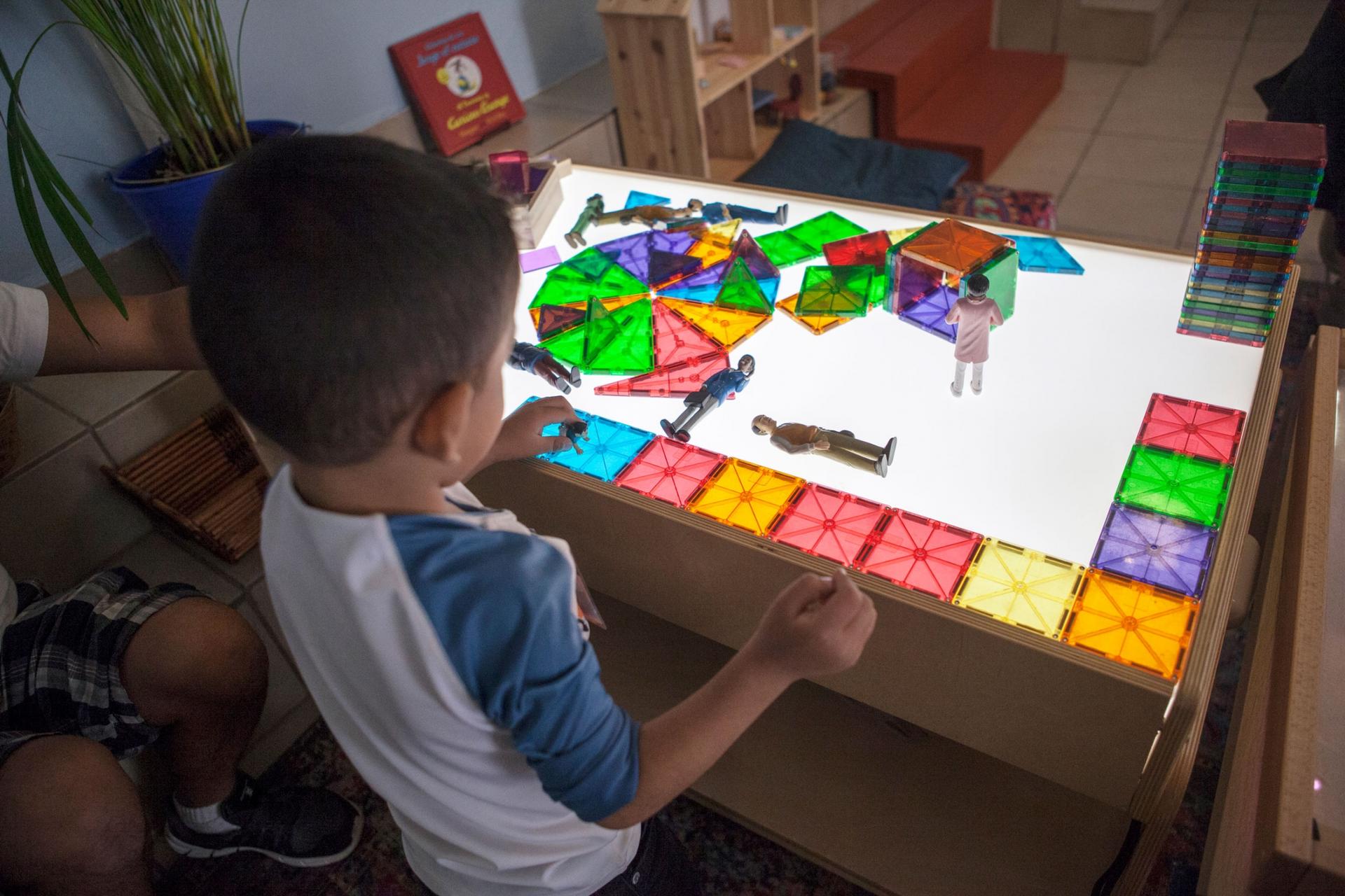 Three-year-old Kevin is shown playing at a table with color-squares illuminated by a table light.