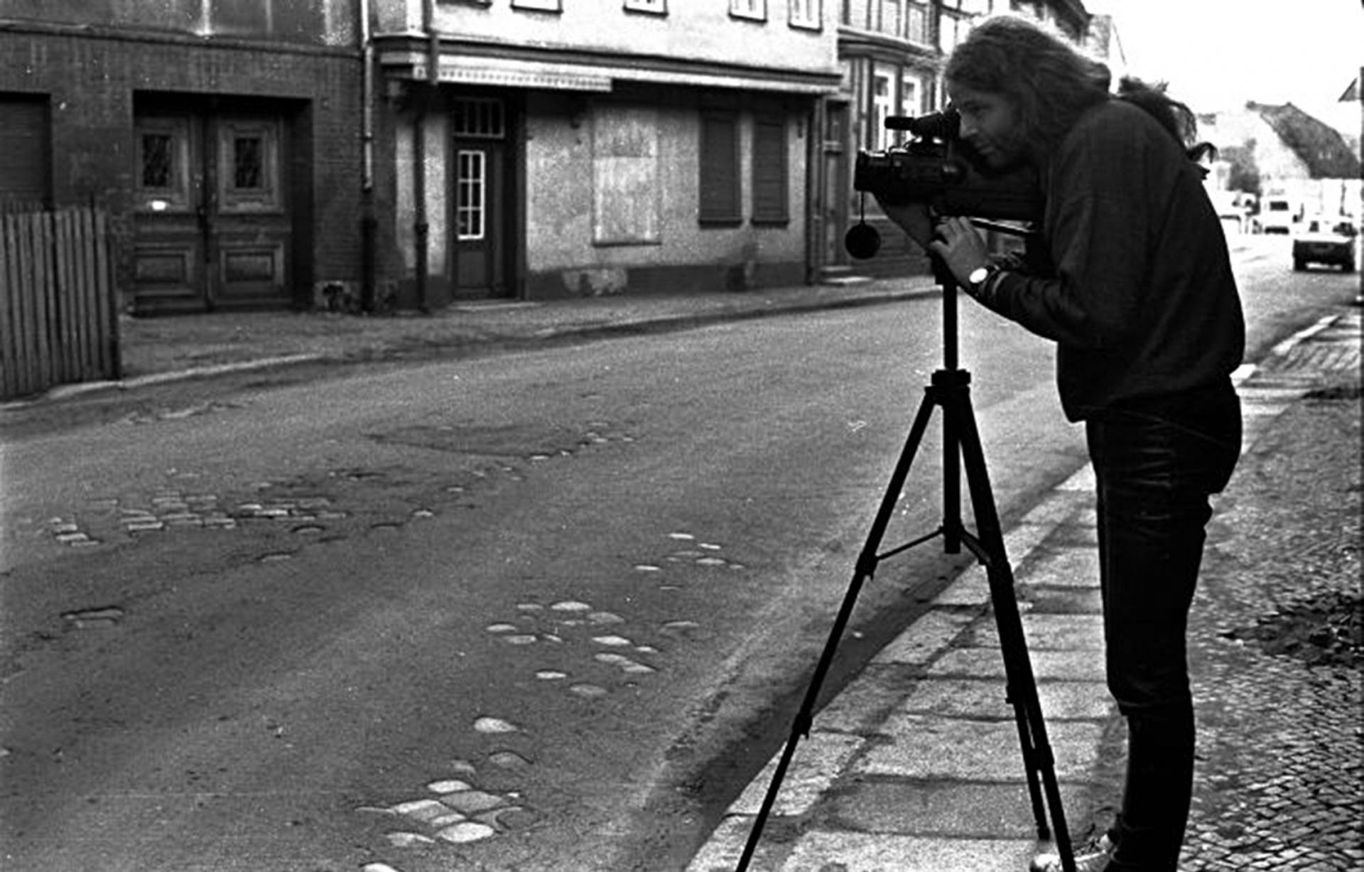 Siegbart Schefke is shown standing behind a camera on a tripod.